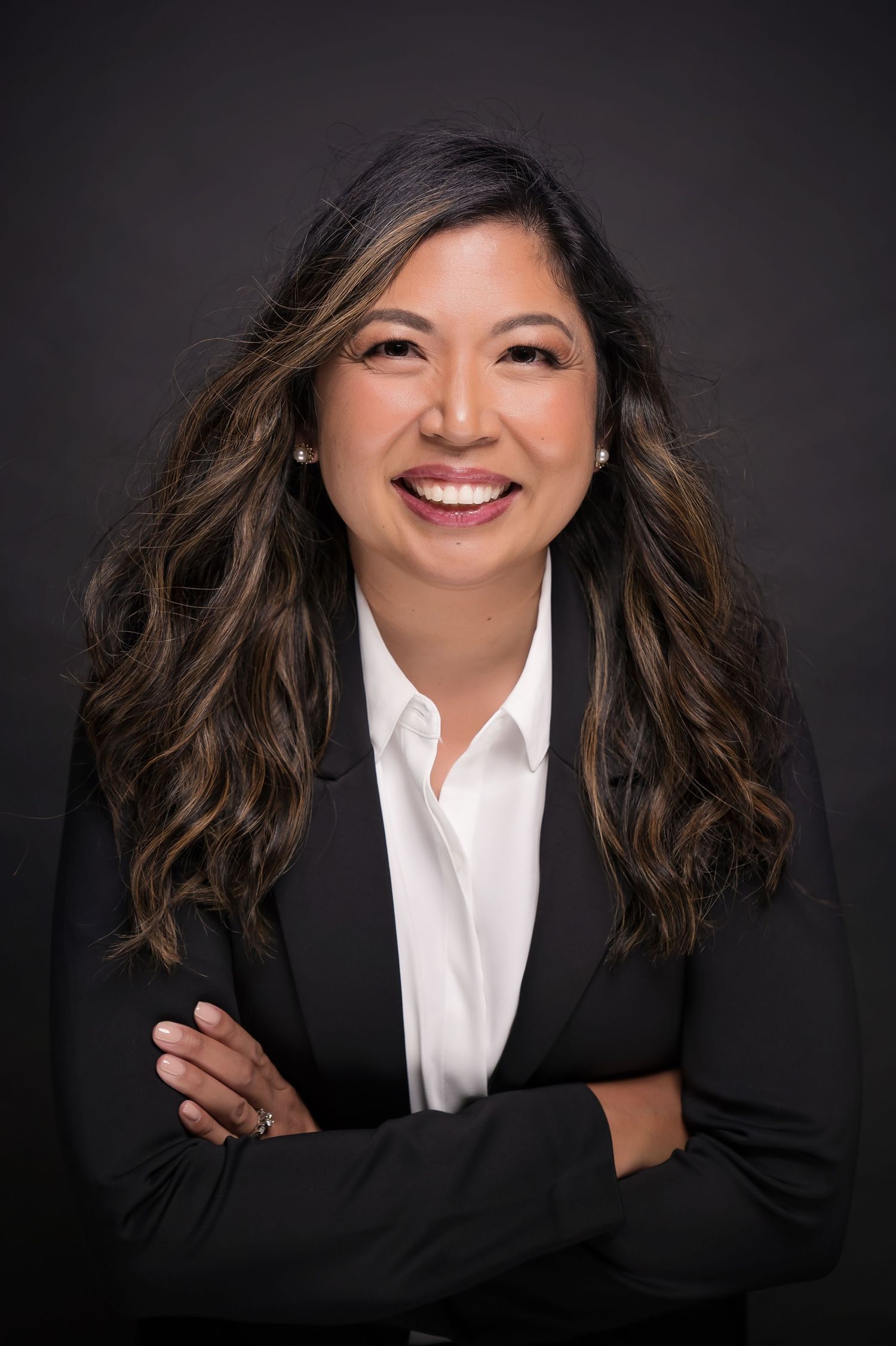 Professional portrait featuring woman in black blazer and white shirt against dark backdrop
