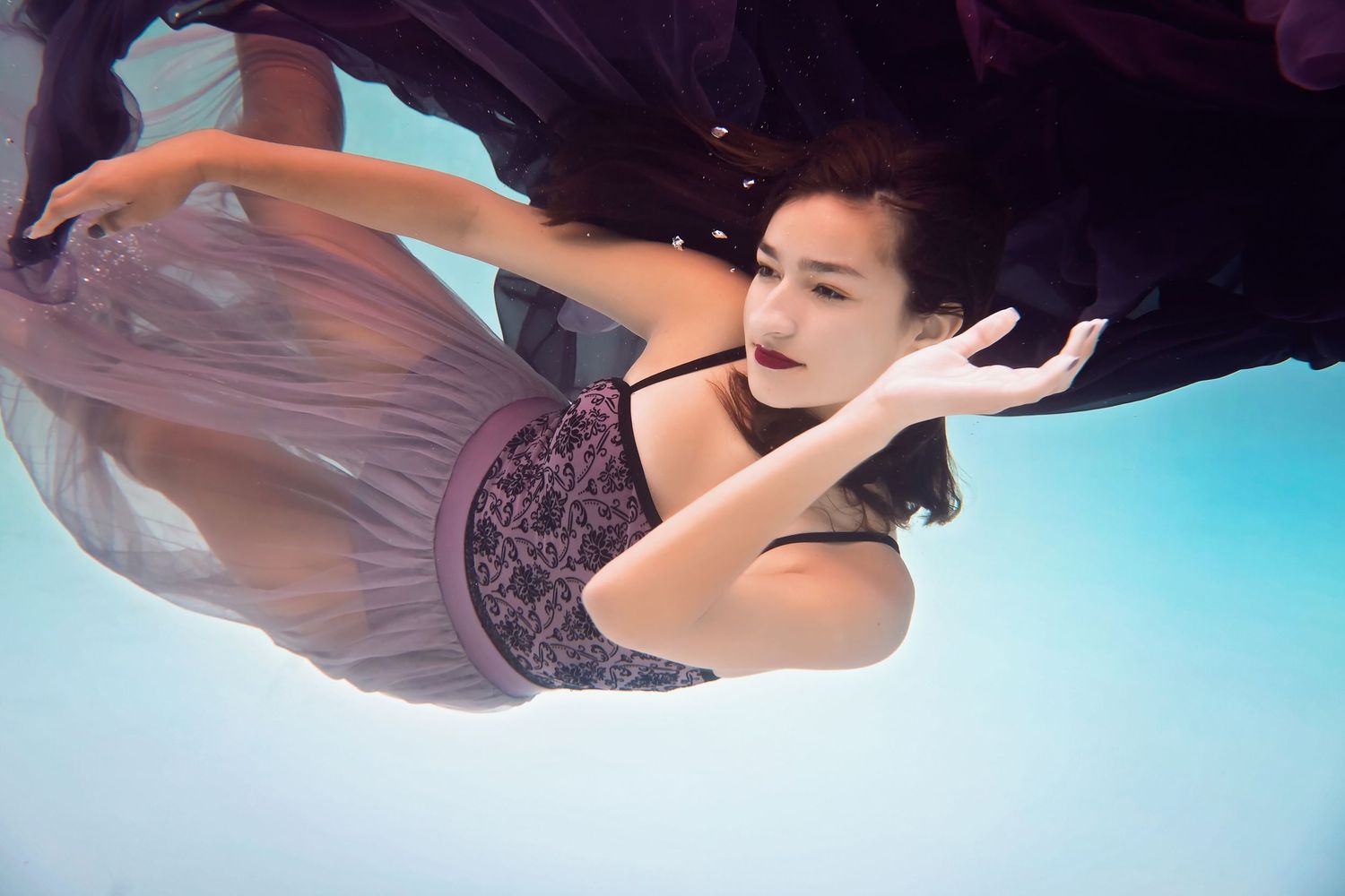 Underwater portrait of woman swimming gracefully with flowing fabric trailing behind