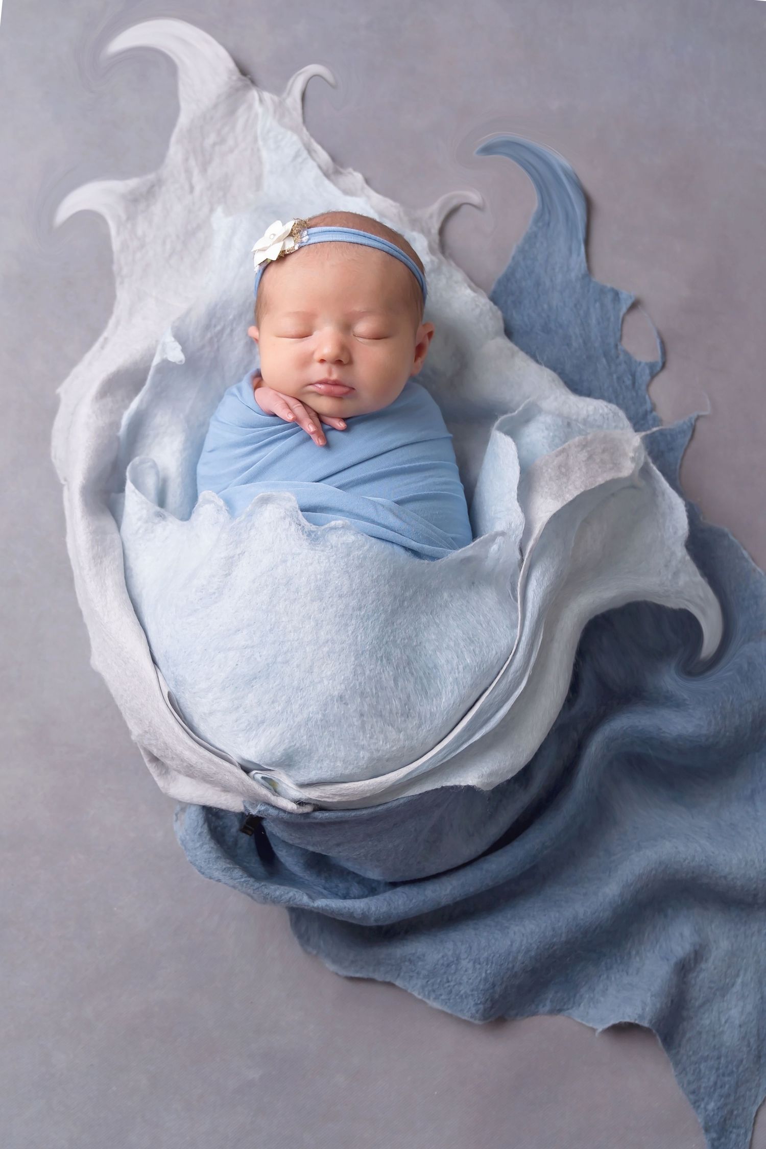 Peaceful sleeping newborn wrapped in blue and white fabrics with artistic lighting. San Diego Newborn Photographer