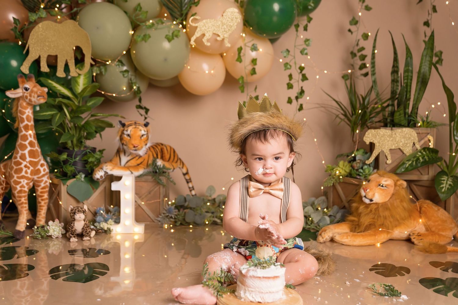 First birthday jungle theme photo setup with balloons, animals and tropical leaves.