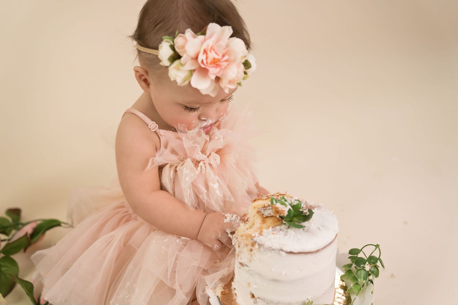Baby milestone photo with pink florals and delicate cake setup against neutral background. San Diego cake smash photographer