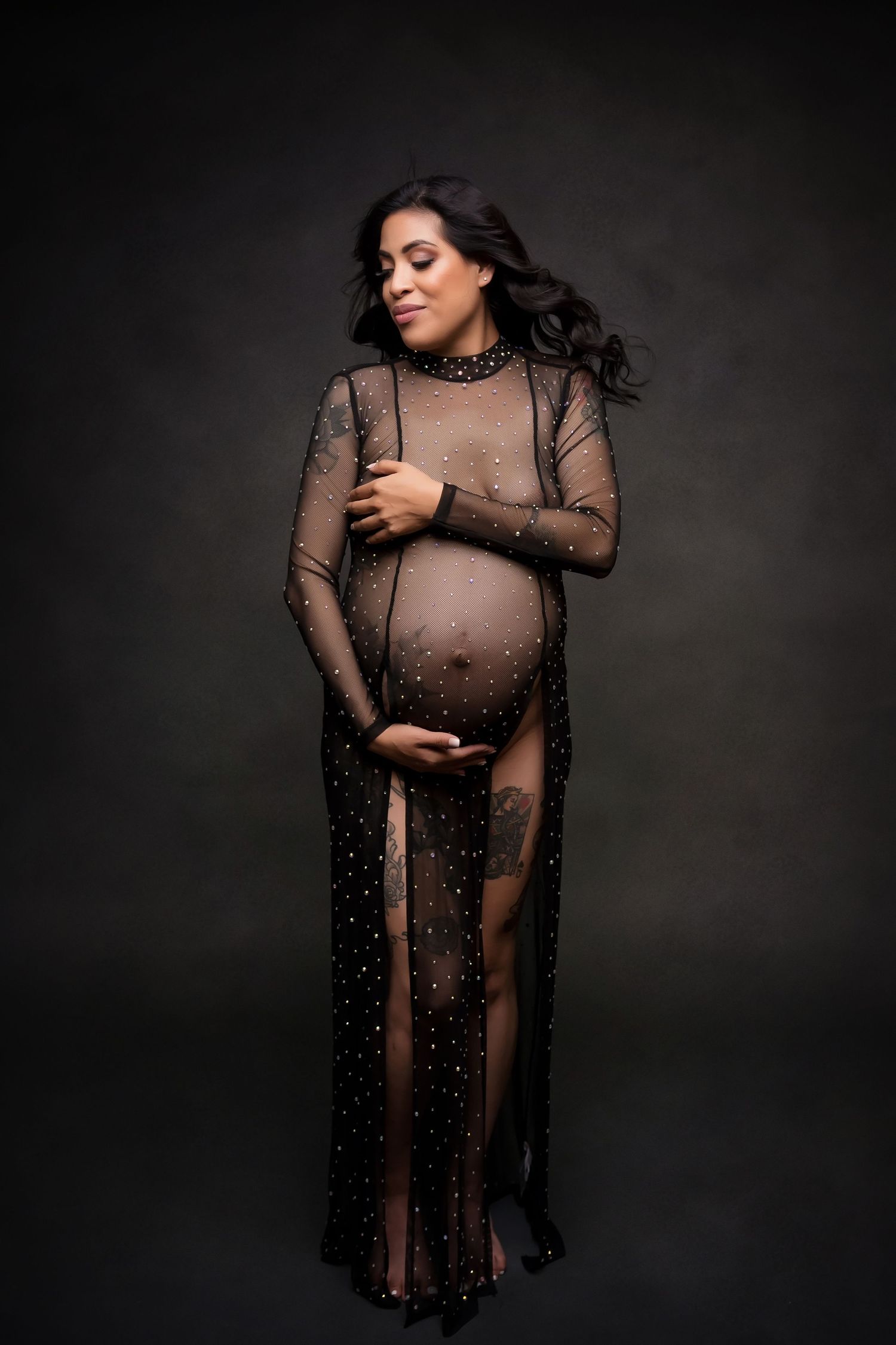 Glamorous maternity portrait in sheer black beaded gown with dark backdrop