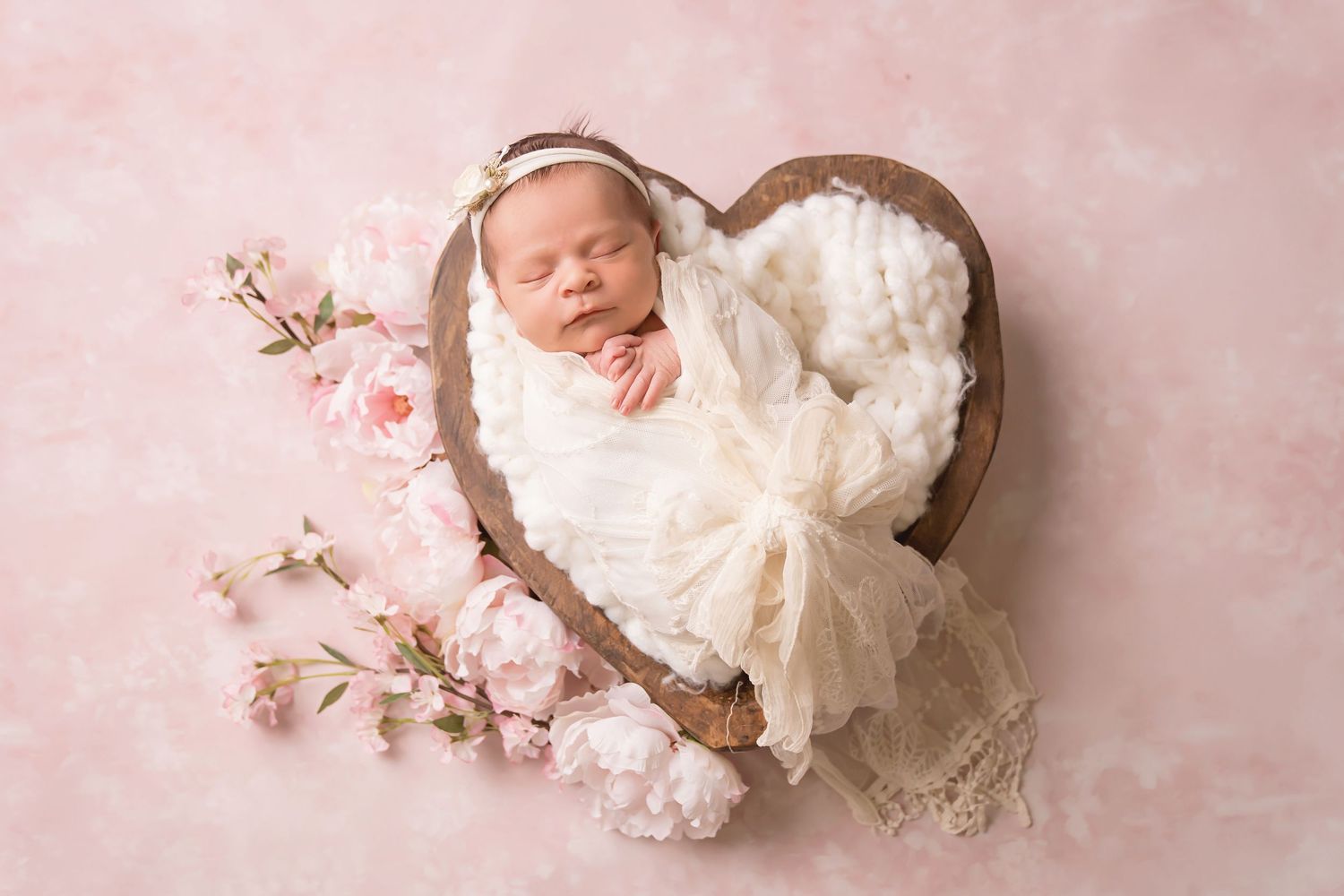Soft pink backdrop with cherry blossoms frames delicate newborn portrait setup. San Diego Newborn Photographer