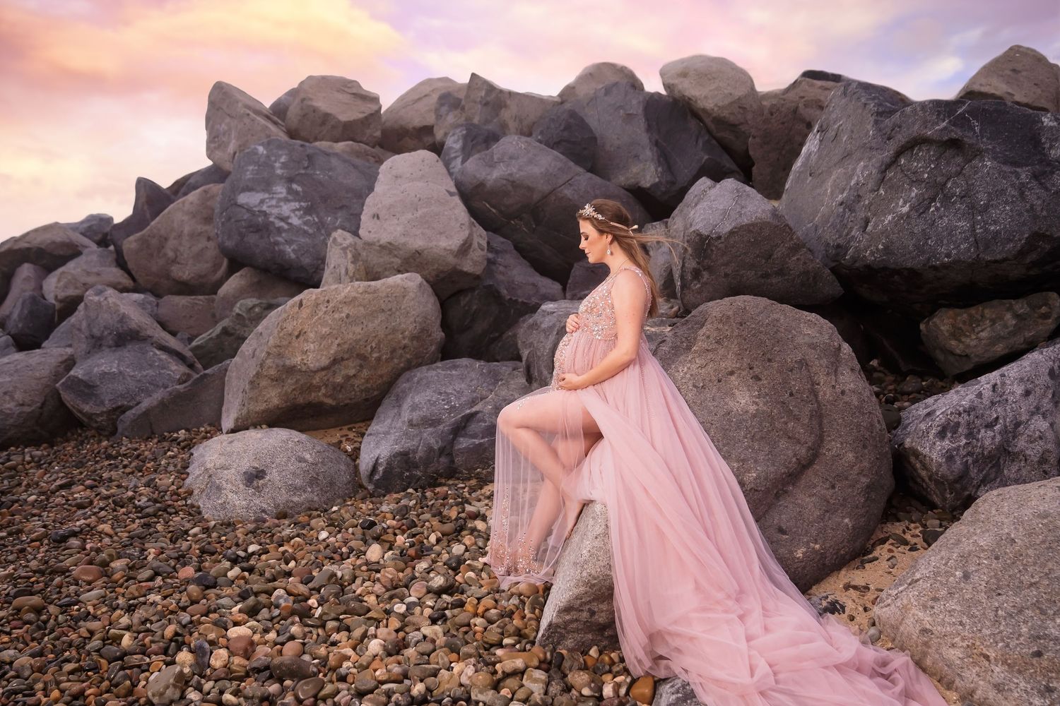 Expecting mother in pink gown poses among coastal rocks at golden hour. San Diego Maternity Photographer