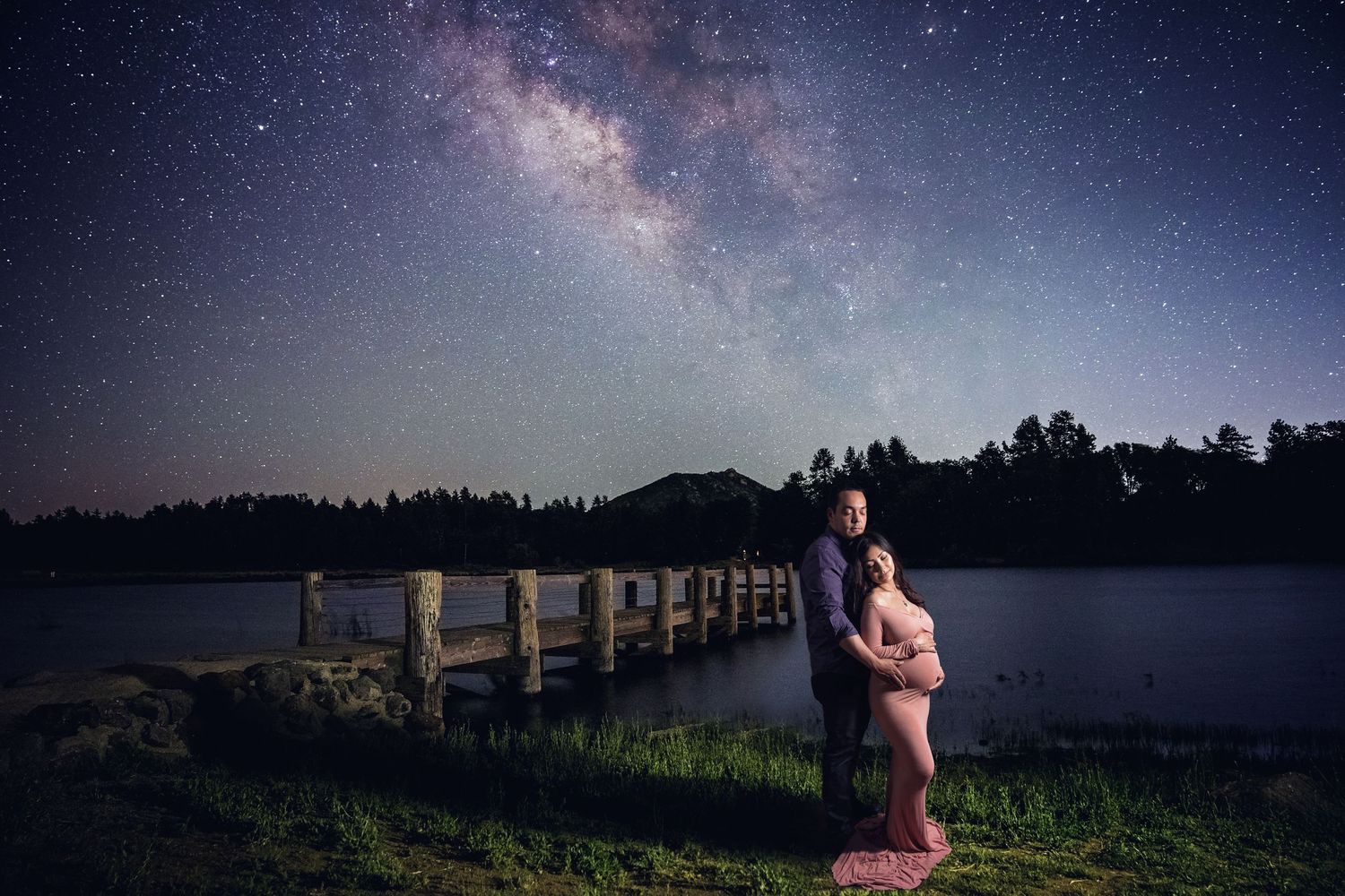 Silhouetted maternity photo against a starry night sky with dramatic lighting and trees in the background.