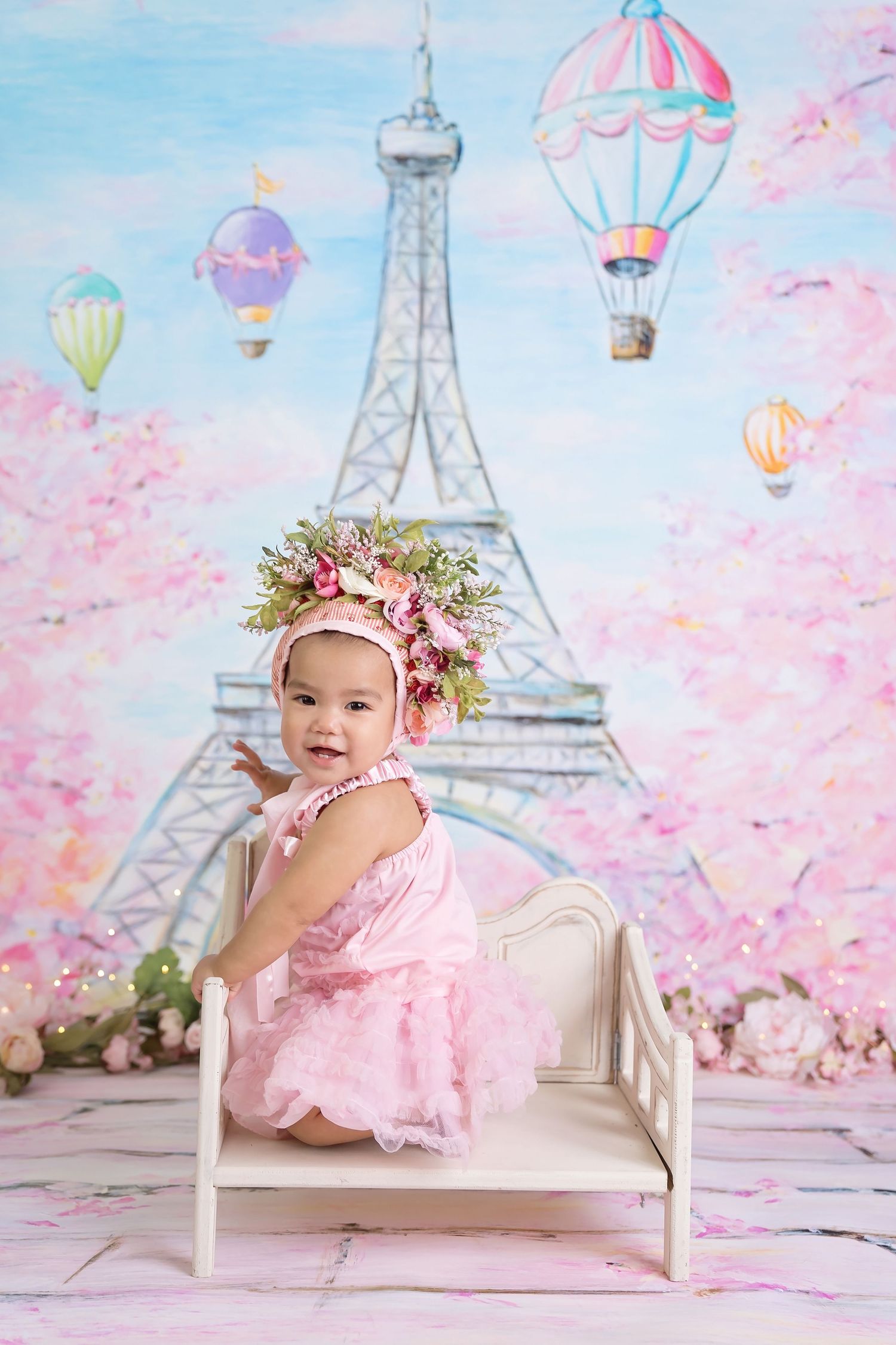 Parisian-themed baby photo set with painted Eiffel Tower and floating hot air balloons in pastel colors. San Diego cake smash photographer