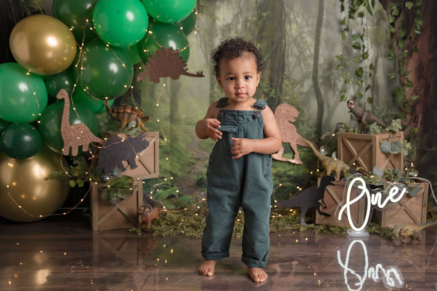 Green and gold balloon decorations with forest-themed backdrop for celebration. San Diego cake smash photographer