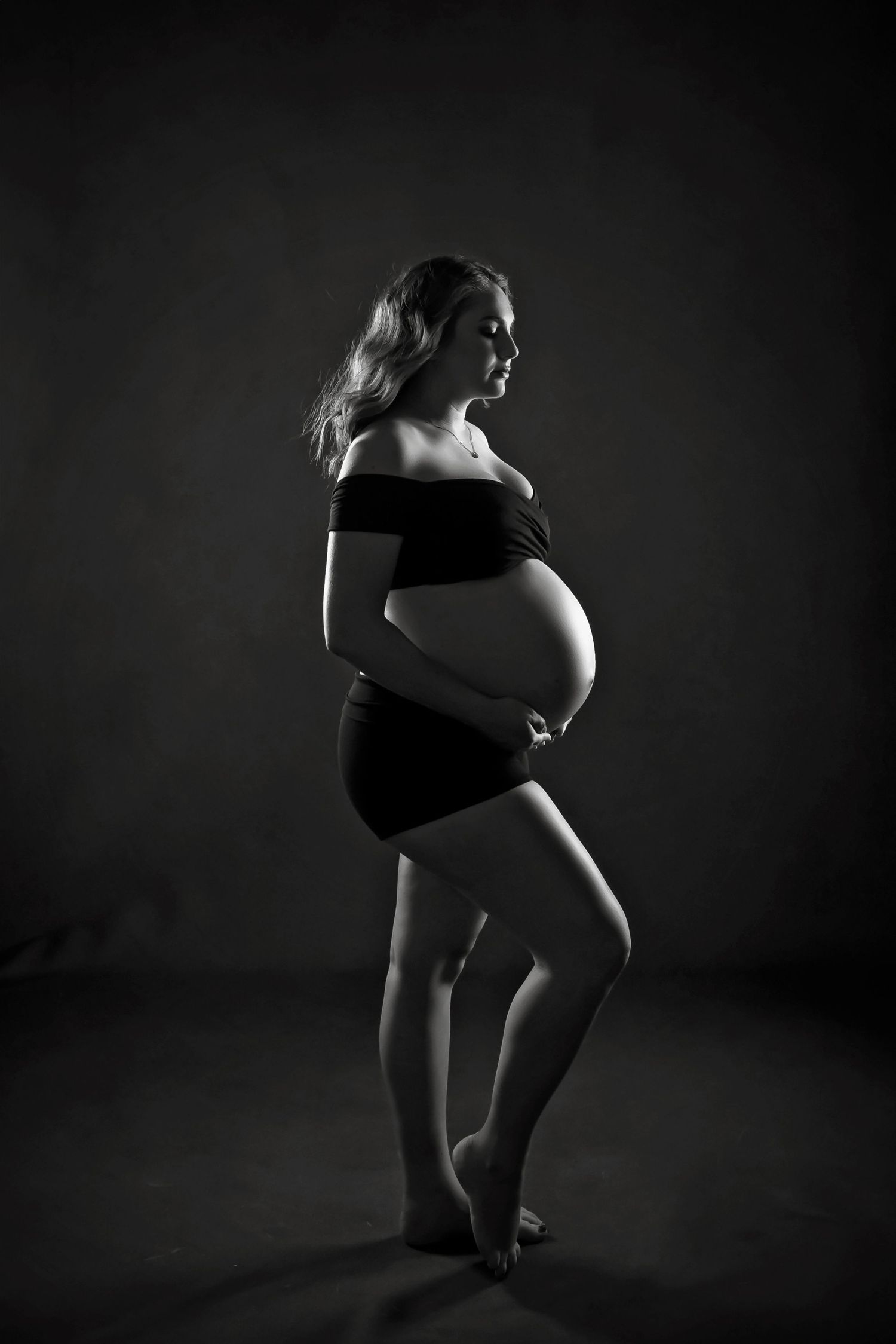 Low-key maternity portrait with dramatic shadows and sculpted lighting