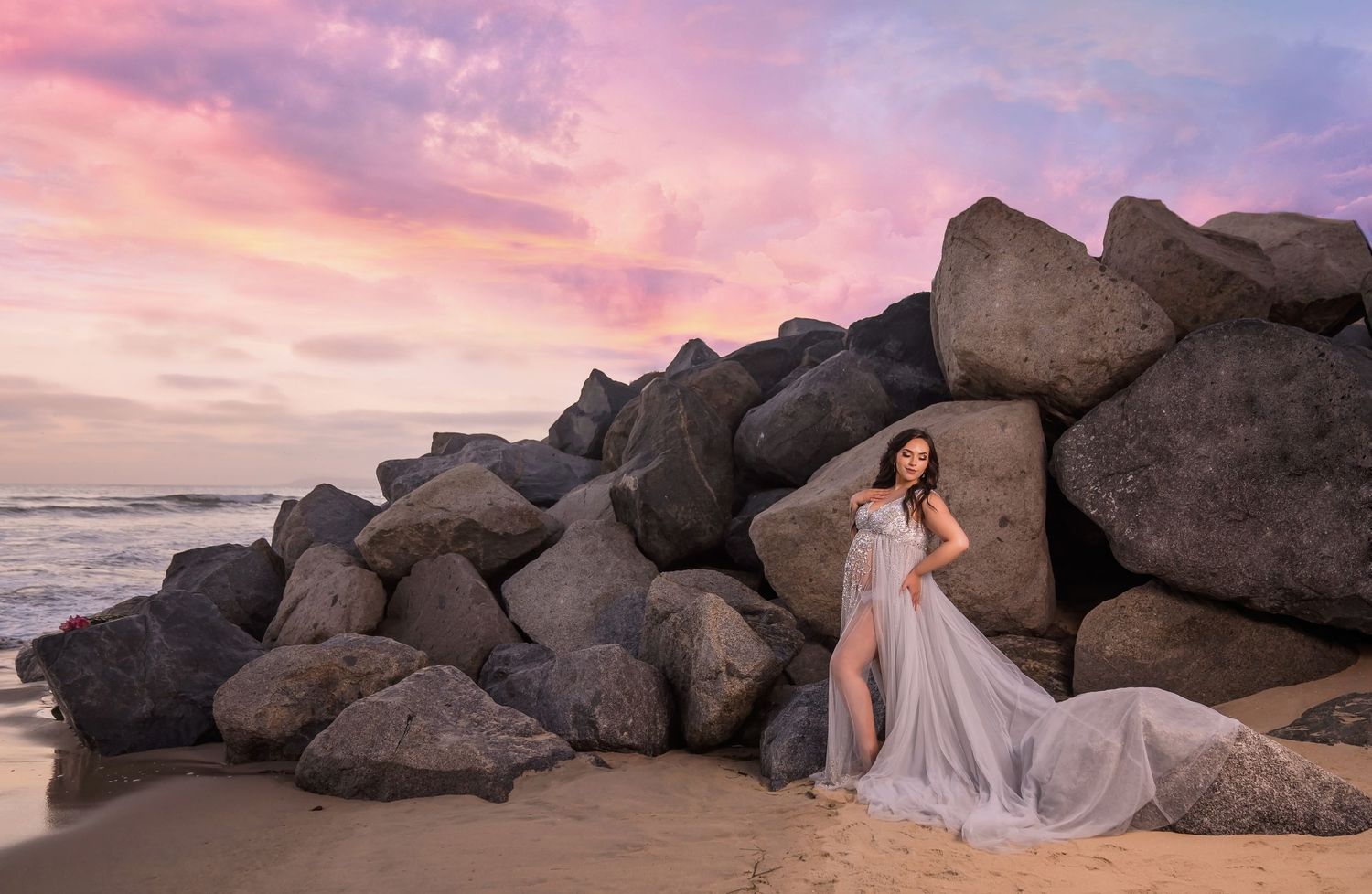 Artistic san diego beach maternity photography with large rocks and pink sunset sky creating dramatic backdrop.