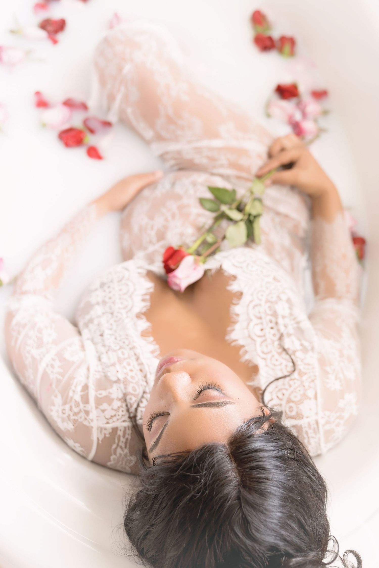 Ethereal milk bath maternity photo with lace dress and scattered rose petals.