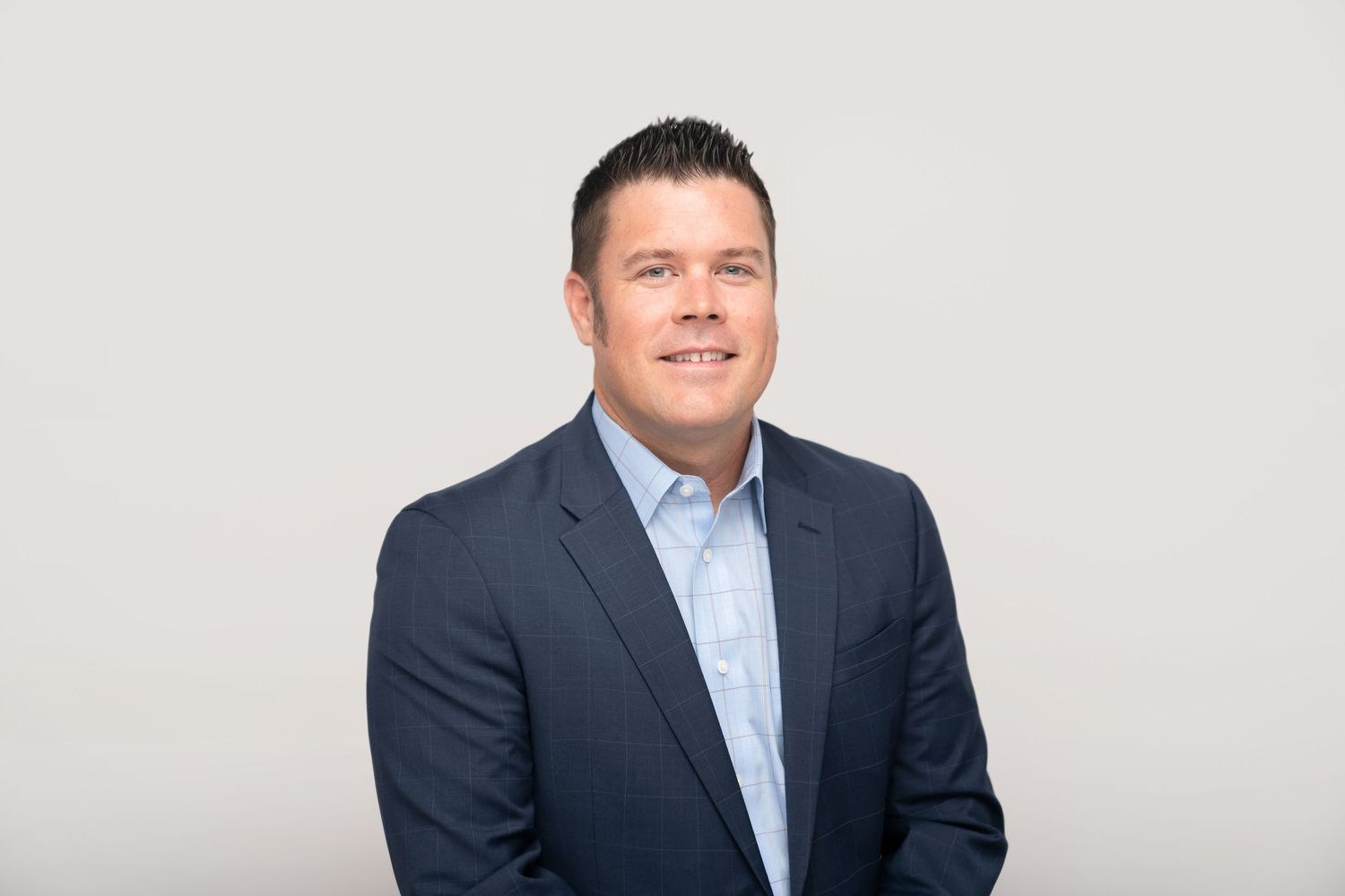 Executive headshot featuring man in navy suit and striped tie against neutral backdrop