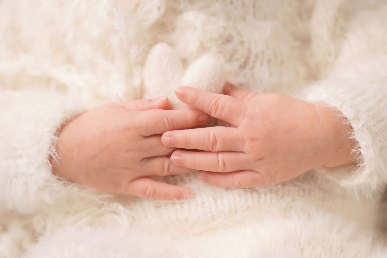 San Diego newborn photographer captures Close-up detail of tiny hands against white textured fabric in newborn photography.