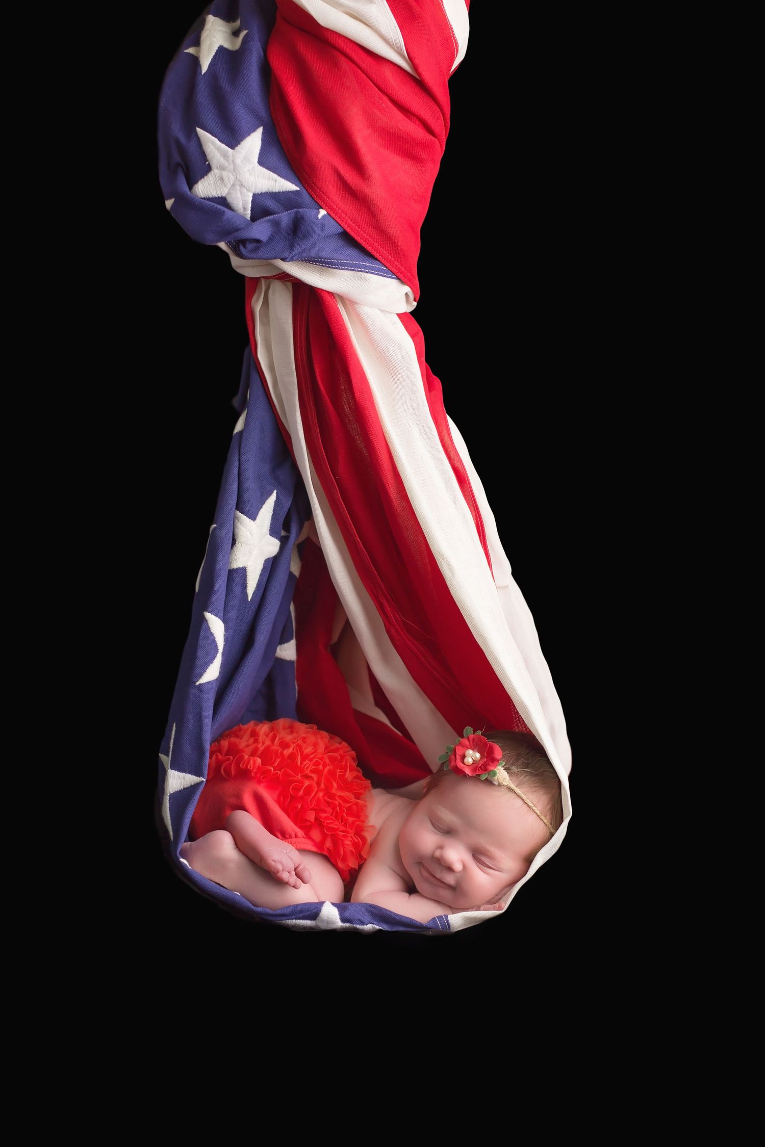San Diego newborn photographer captures Sleeping newborn wrapped in American flag against black background.