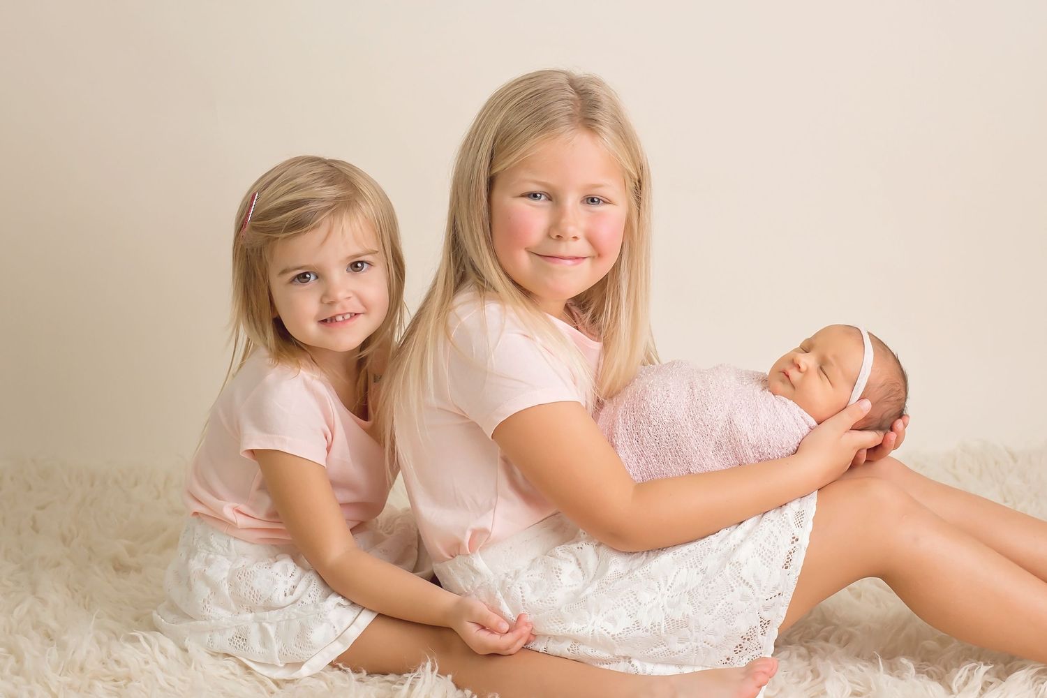 Sweet siblings in white dresses posing together on cream colored background. San Diego Newborn Photographer
