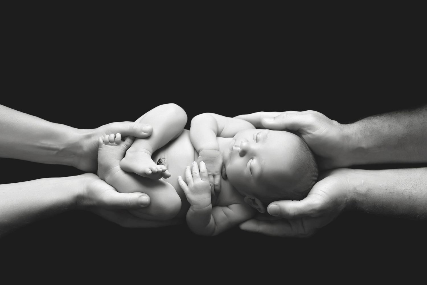 Black and white image showing hands gently cradling a baby. San Diego Newborn Photographer