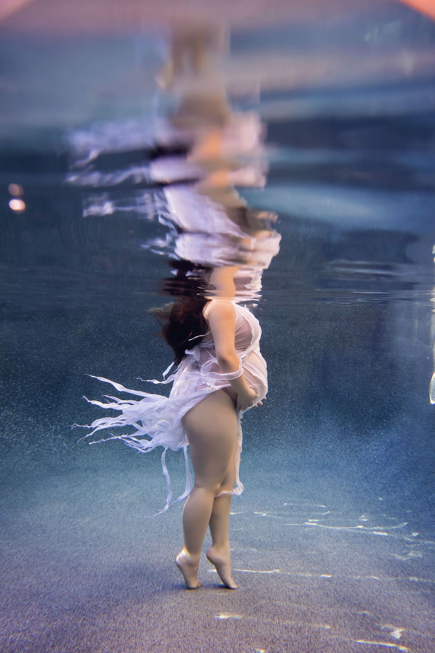 Underwater view pregnant woman walking on pool floor with rippling reflections