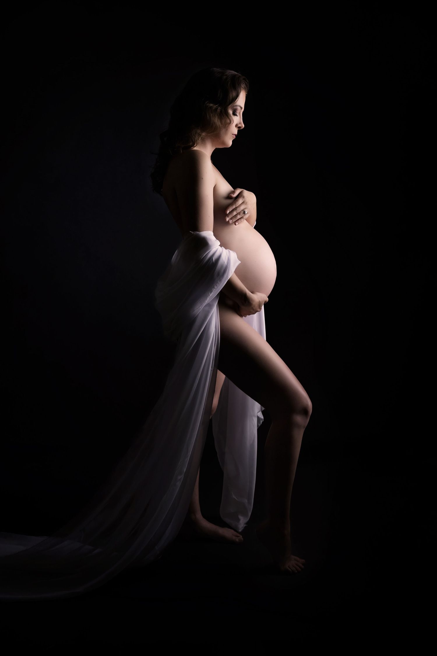 Low-key maternity portrait with flowing white fabric in a dark studio setting