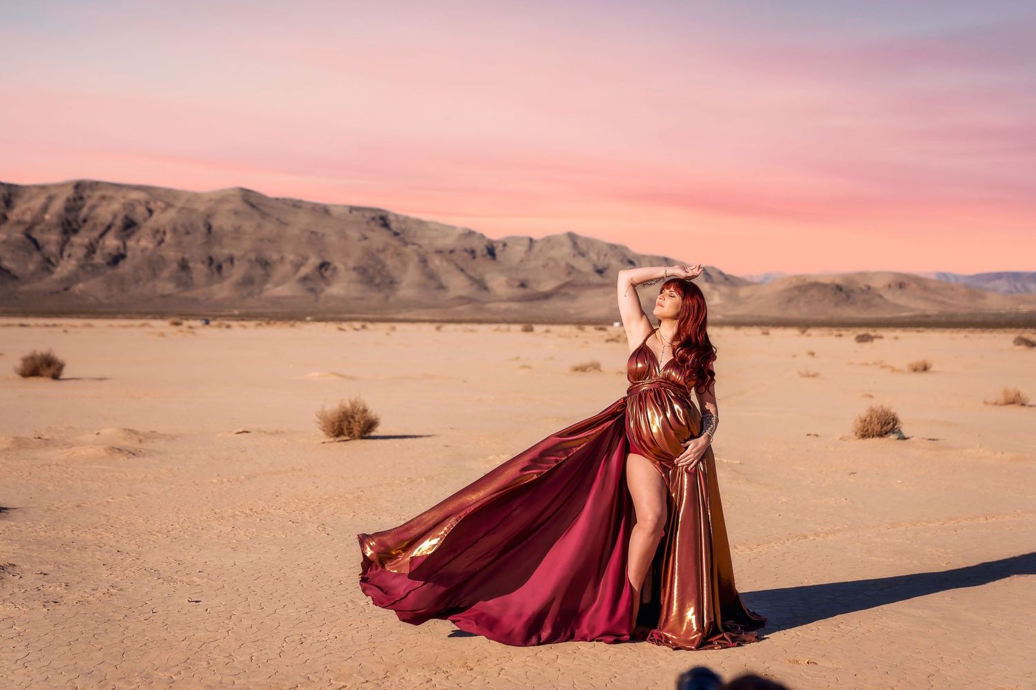 A flowing burgundy dress billows dramatically across a desert landscape at sunset. San Diego Maternity Session