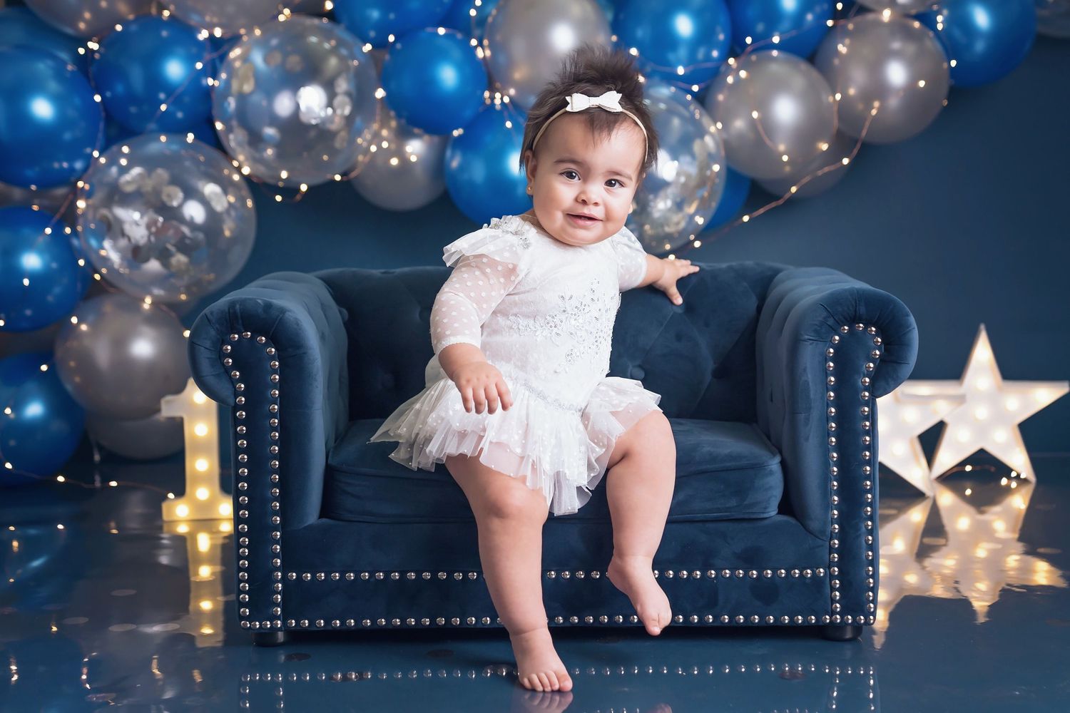Birthday photoshoot scene with illuminated number one, blue balloons and star decorations.