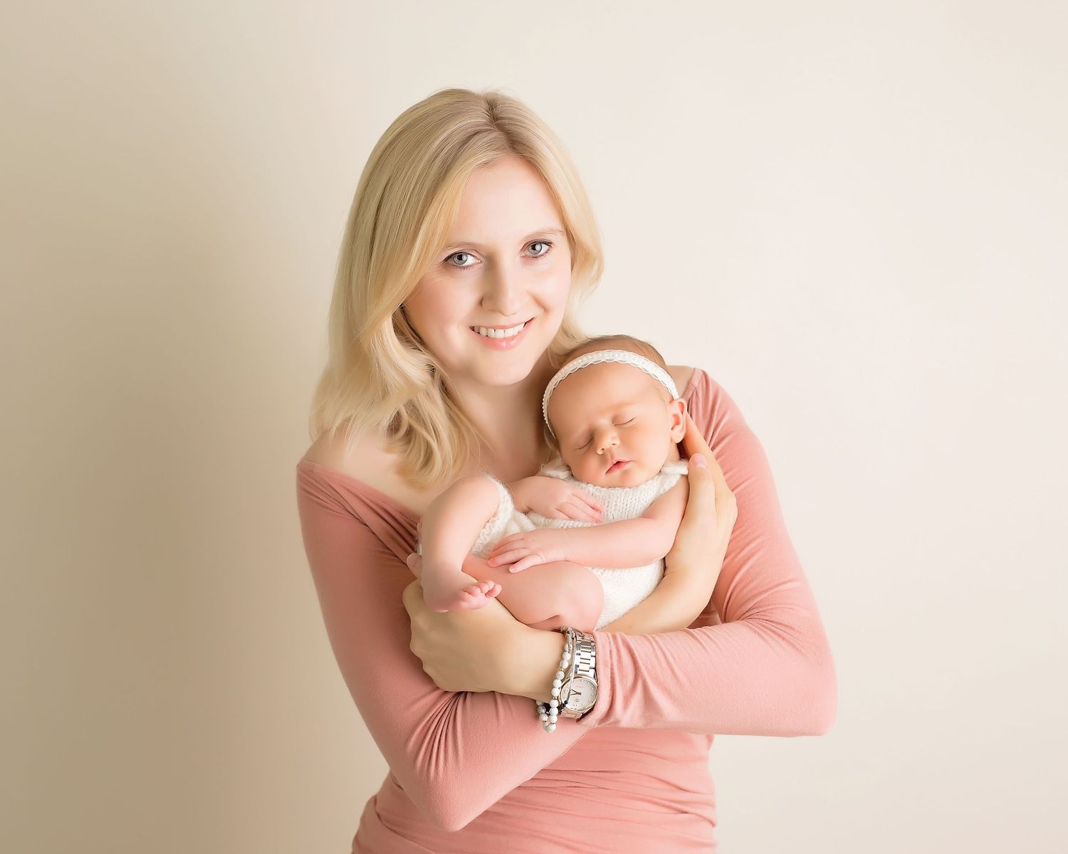 Mother in coral top holding sleeping newborn during studio photography session. San Diego Newborn Photographer