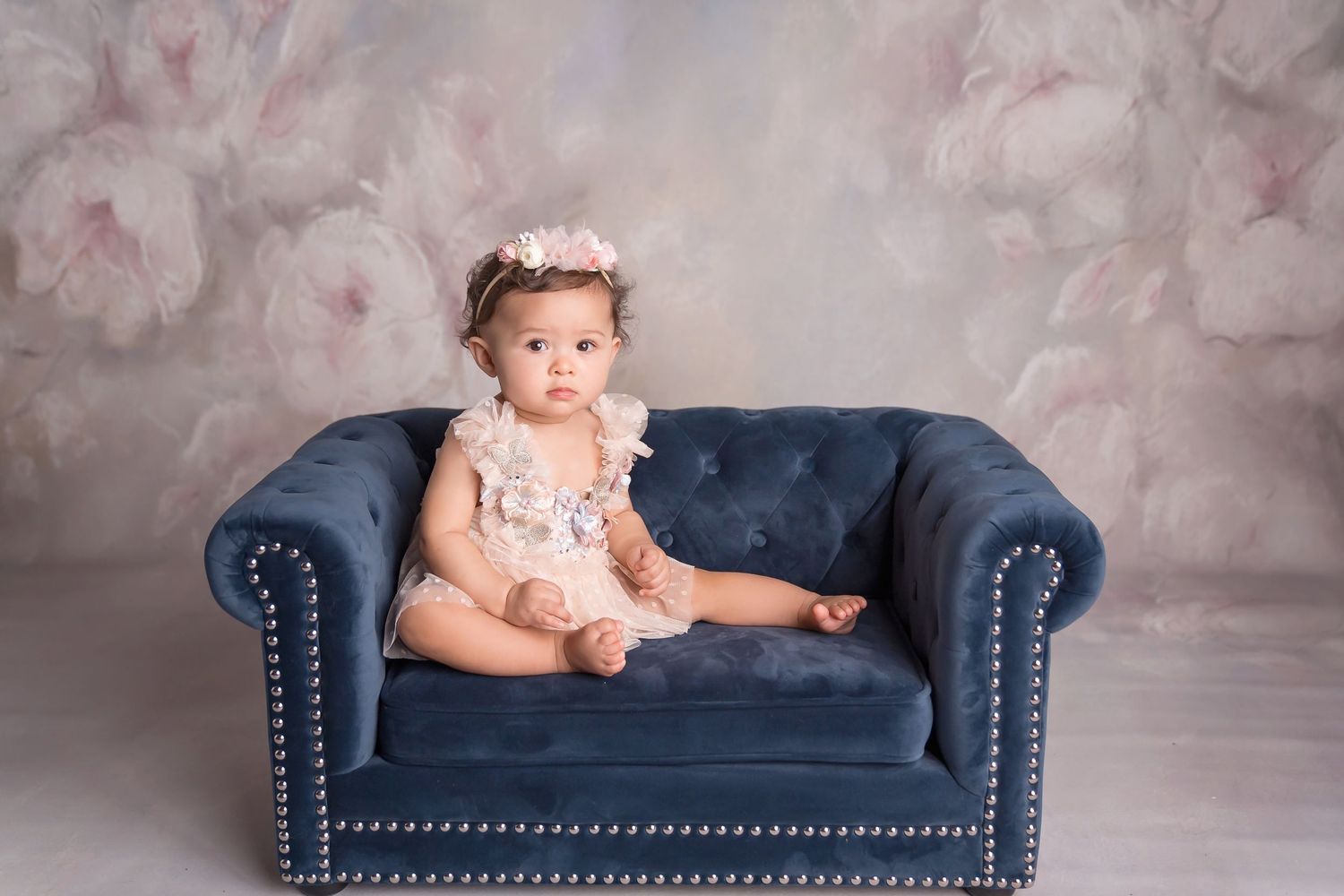 Navy blue tufted chaise lounge against a soft pink backdrop in a studio setting.