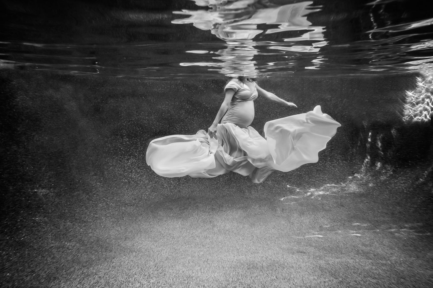 Grayscale underwater maternity photo showing graceful movement through water with flowing material.