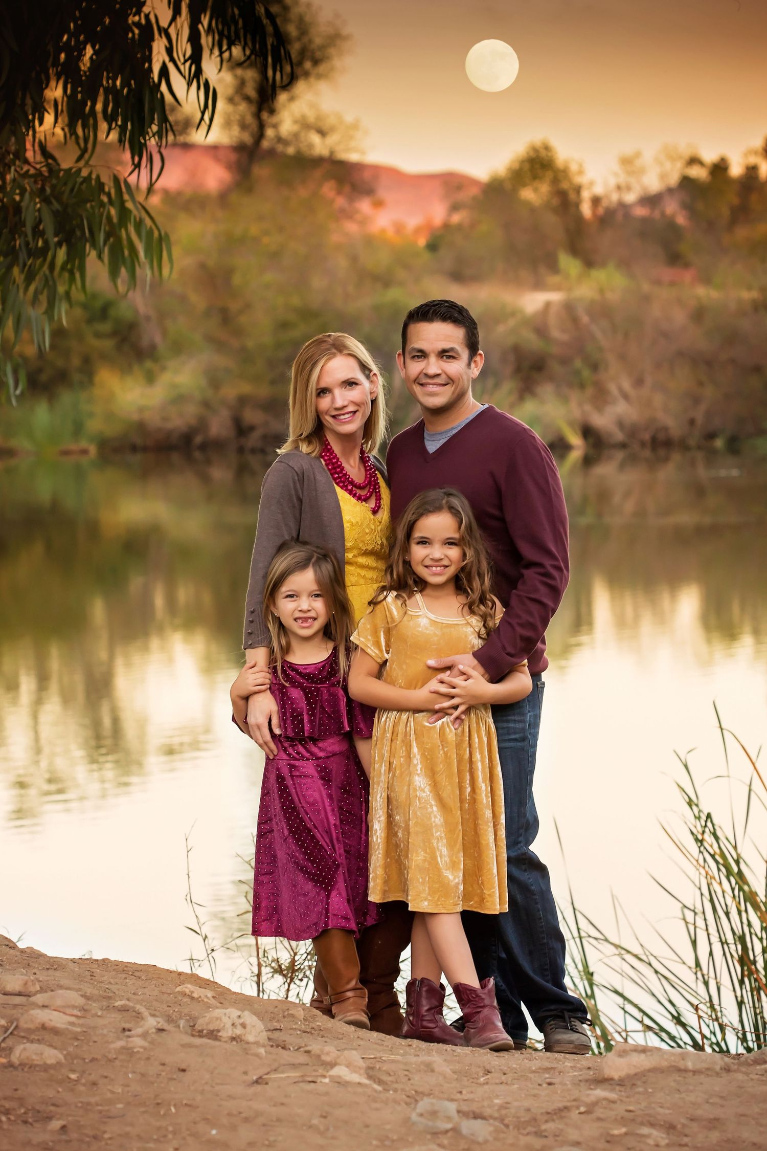 Family portrait by a lake at sunset wearing coordinated burgundy and gold outfits