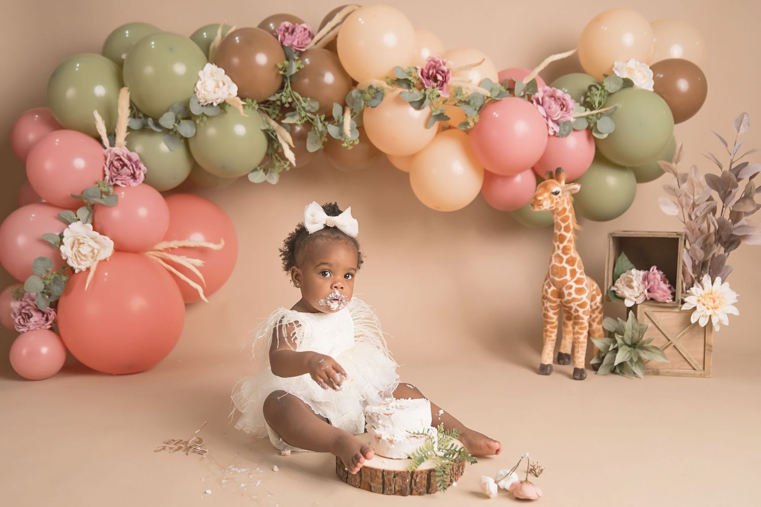 Floral backdrop with pink and sage green balloons creates an elegant first birthday photo setup. San Diego cake smash photographer