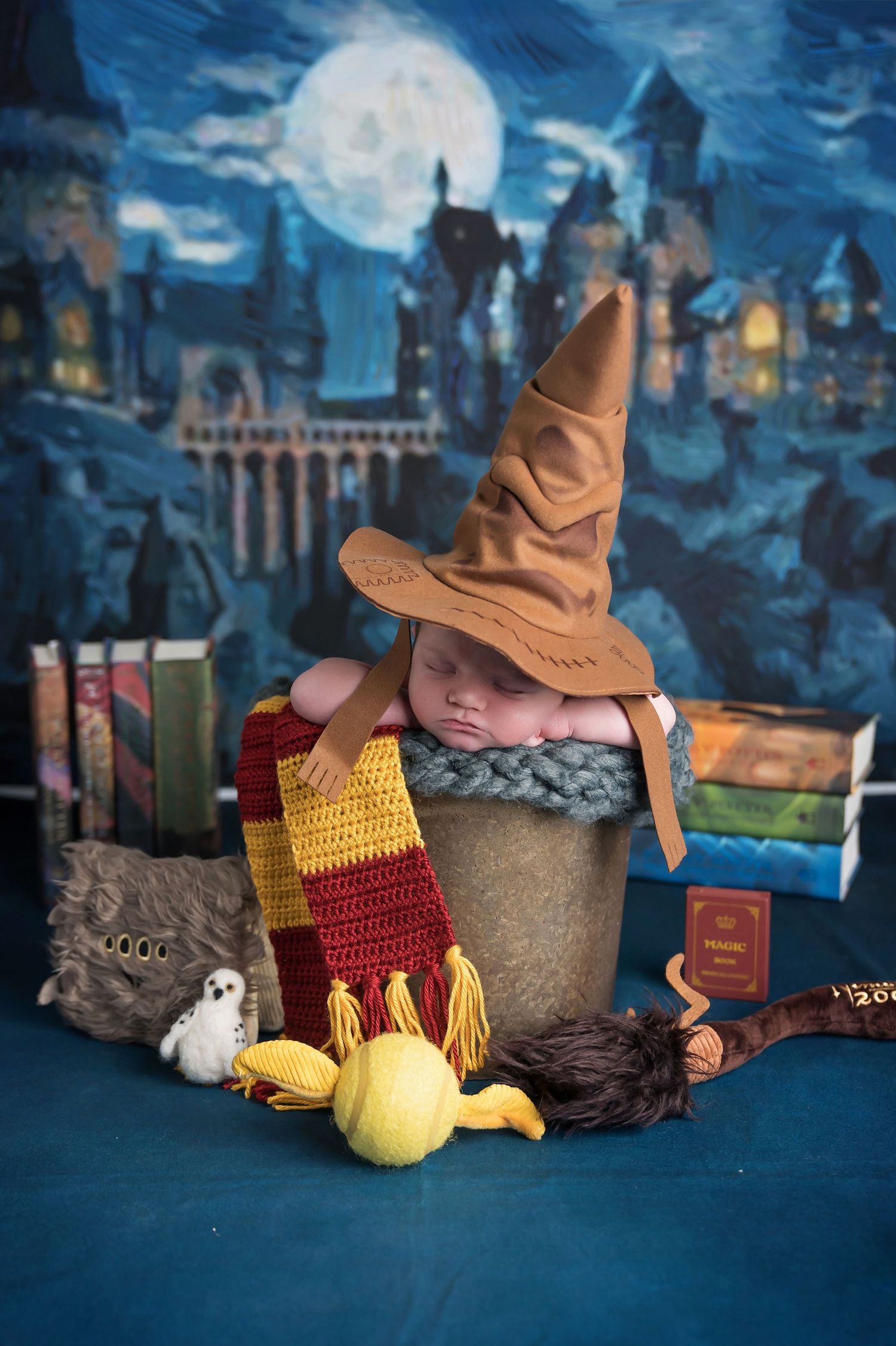 Newborn photography setup with Harry Potter themed props including wand, scarf, and sorting hat against magical backdrop. San Diego Newborn
