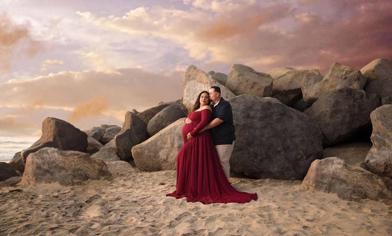 Artistic maternity portraits with burgundy dress against rocky beach setting. San Diego Maternity Photographer
