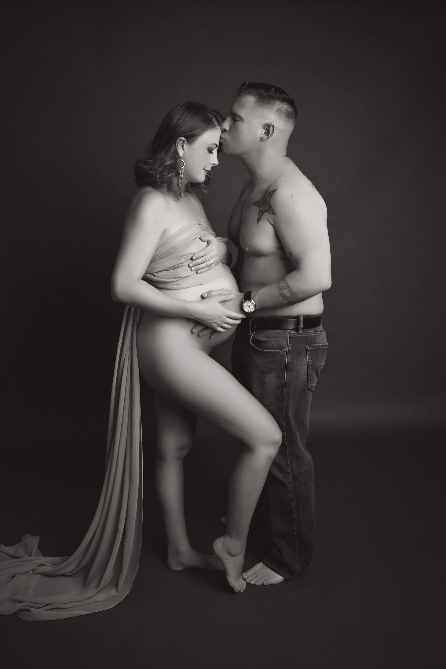 Artistic black and white maternity portrait with flowing fabric and intimate pose.