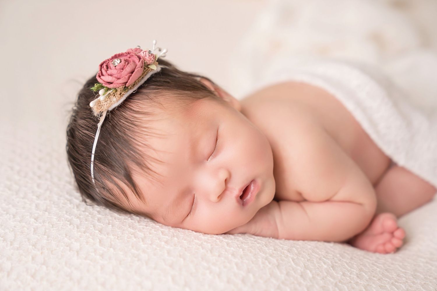 Delicate newborn portrait with pink floral accessories against cream background. San Diego Newborn Photographer