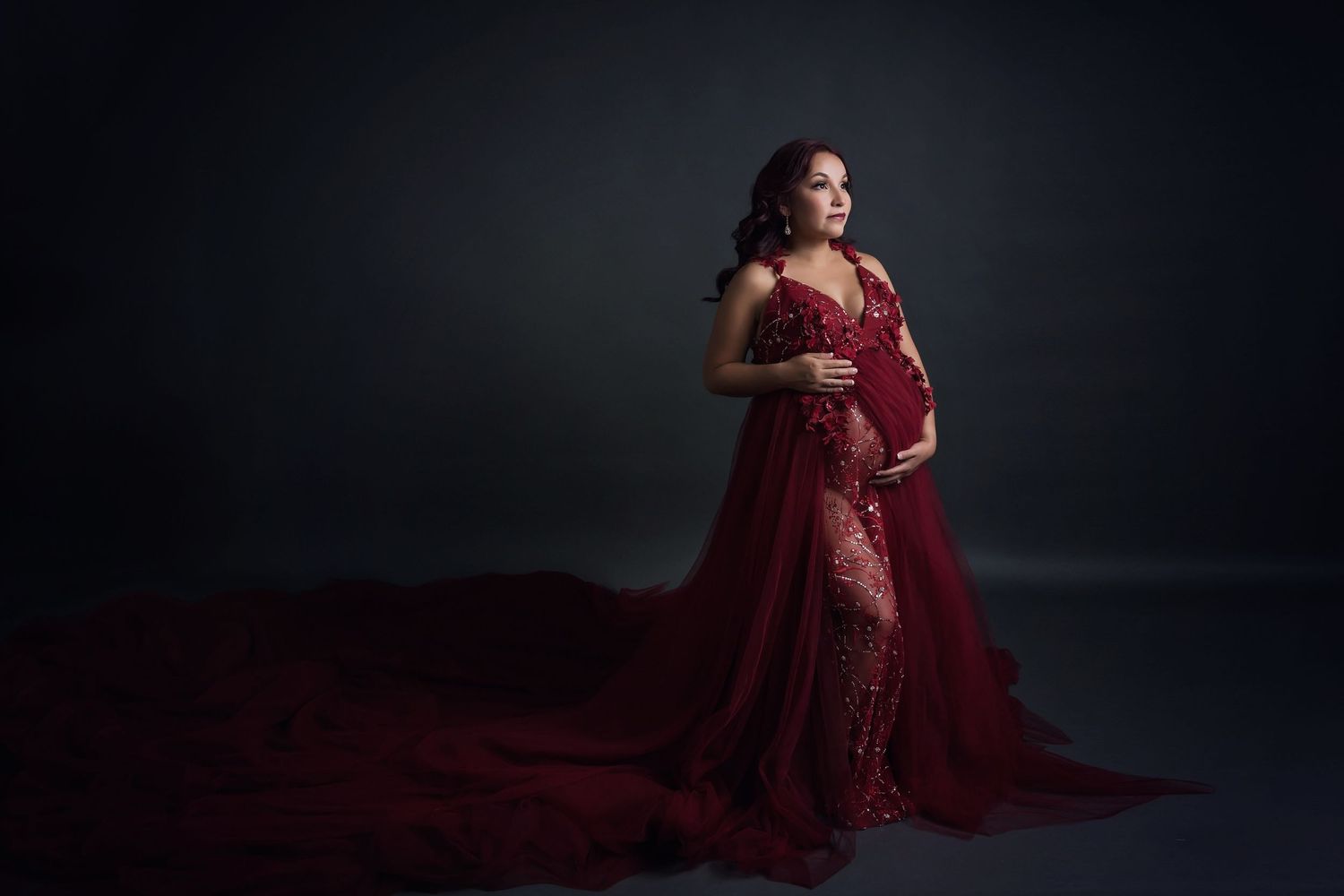 Elegant maternity photography session featuring a flowing burgundy lace gown.