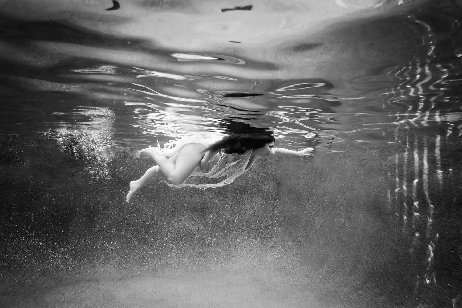 Black and white underwater portrait highlighting movement and reflective water surfaces