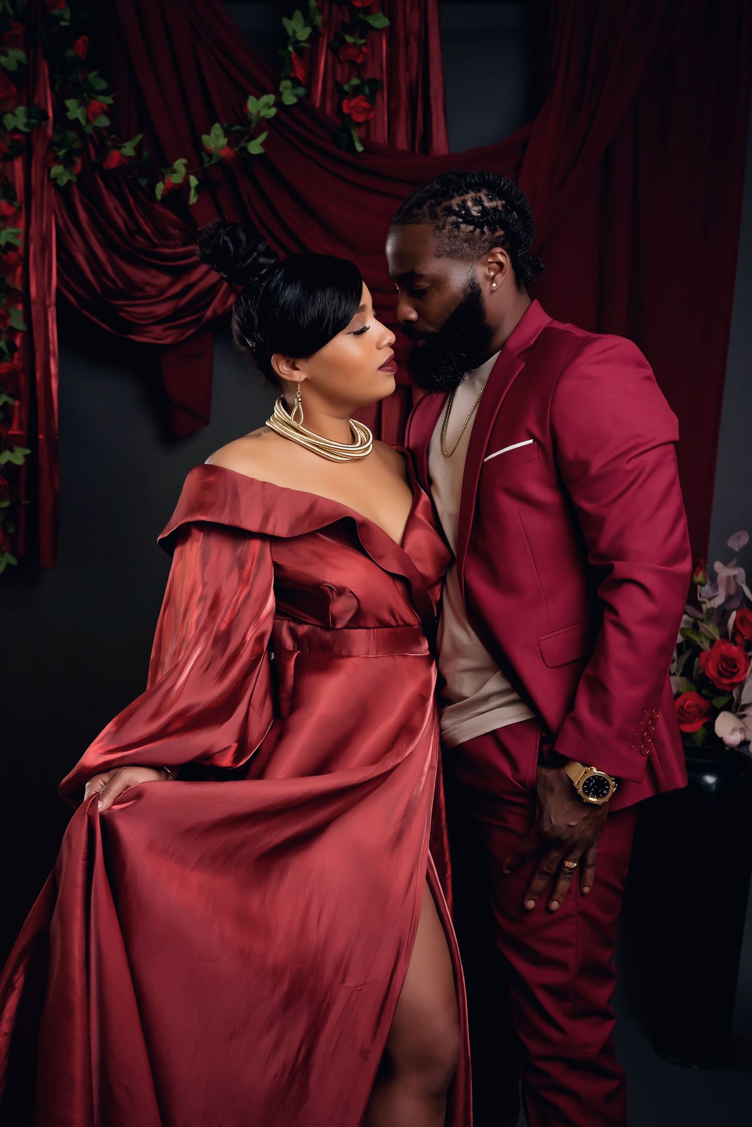 Romantic family portrait in formal attire set against deep red curtains with dramatic studio lighting