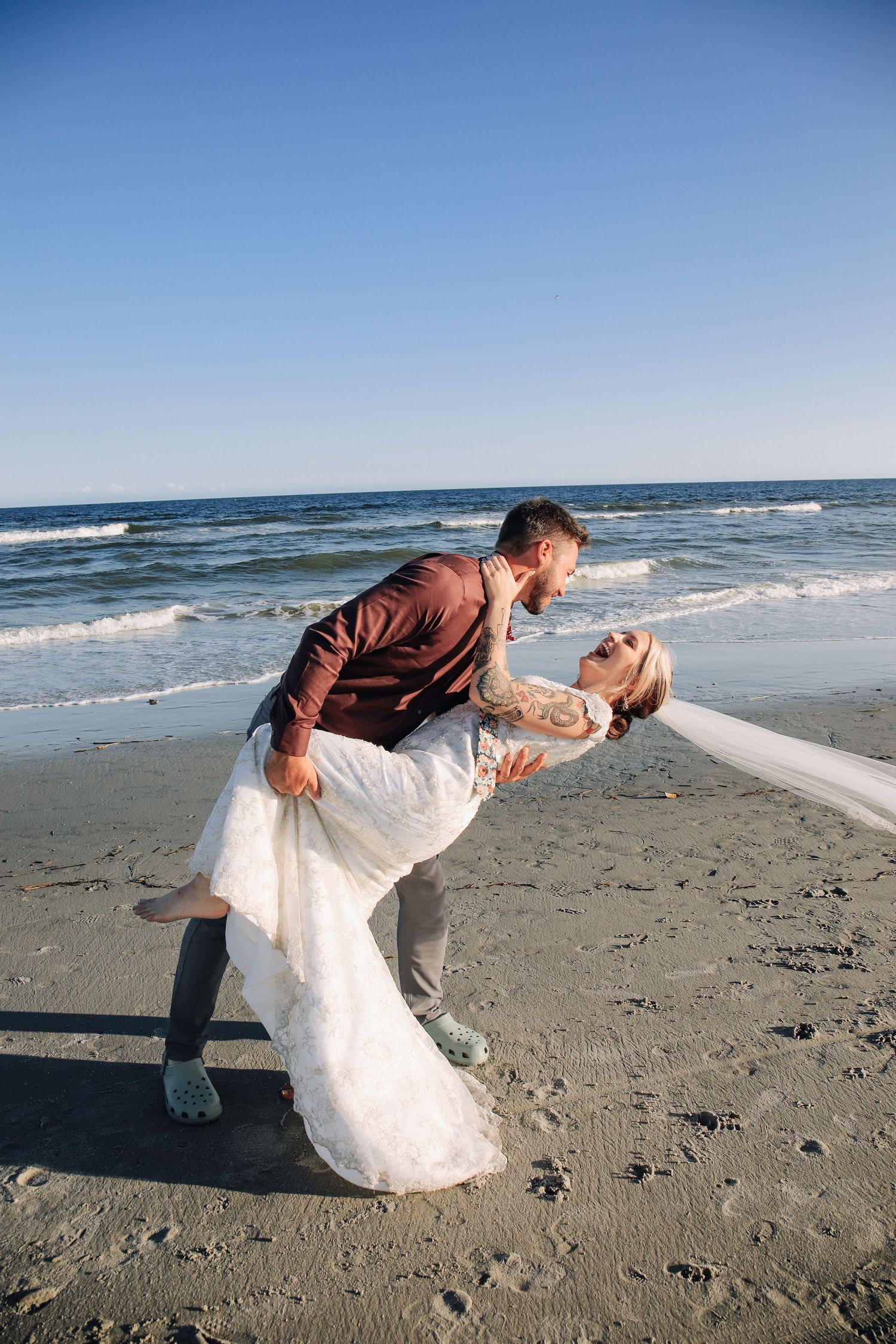 Newly married couple walks along beach for after wedding photography.