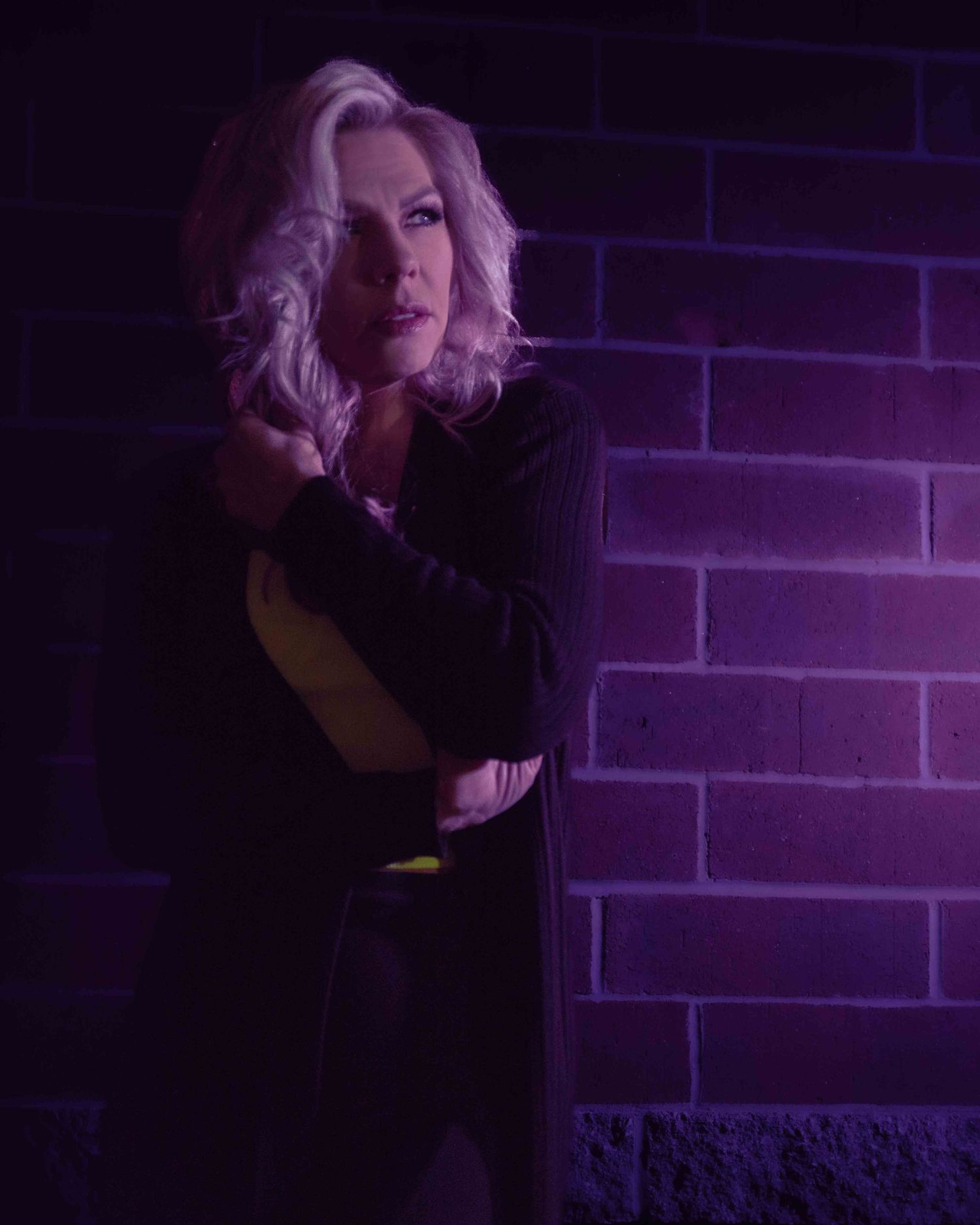 Blonde beauty model photo with a brick wall and purple lighting