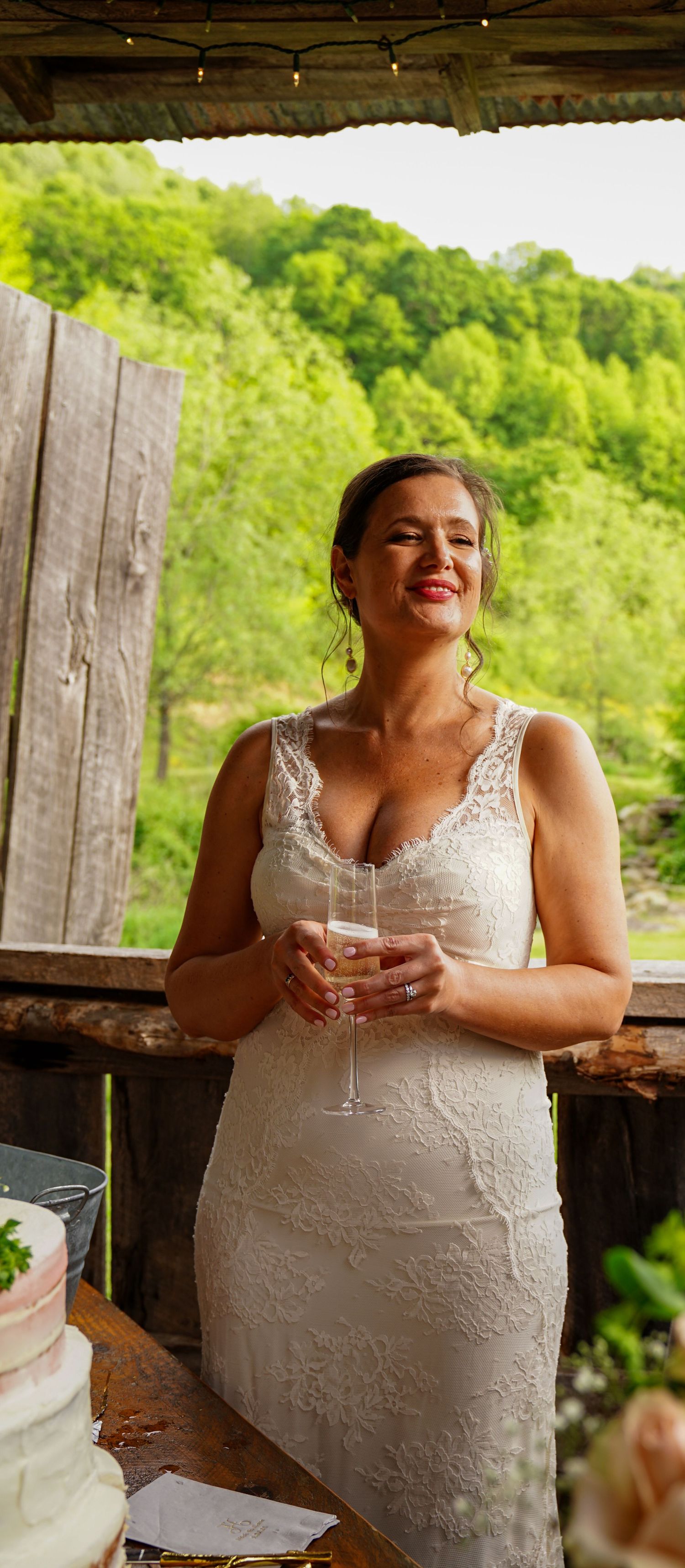 A joyful moment captured in a white lace wedding dress against a rustic wooden backdrop with green foliage.