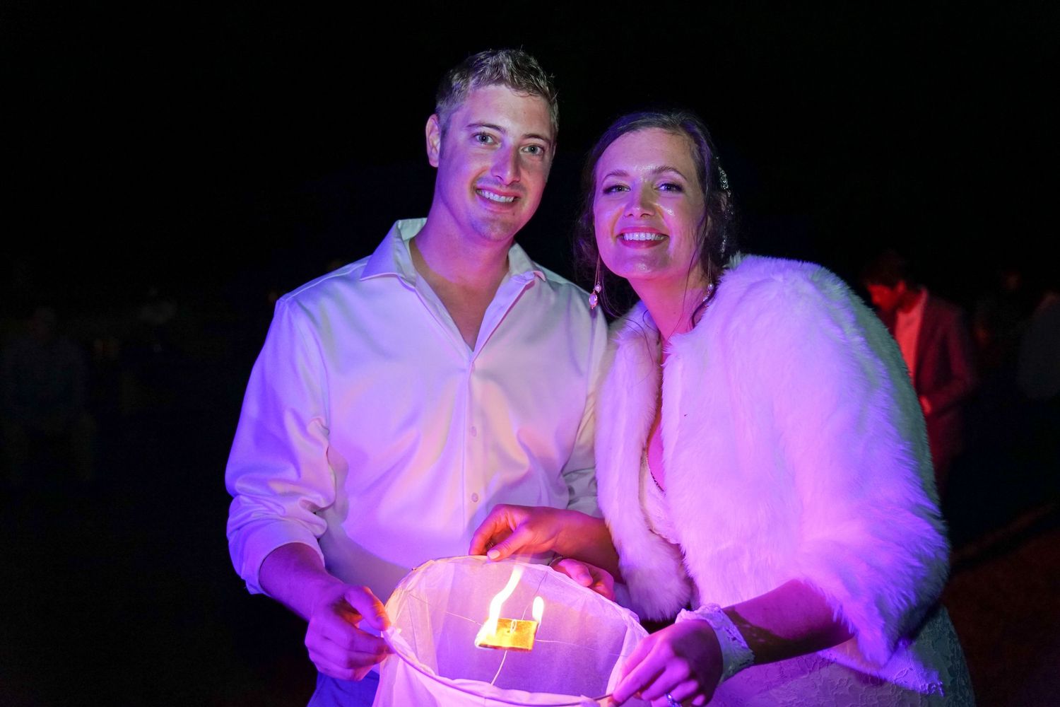 People in white shirts dance and celebrate at a nightclub under pink and purple lighting effects.