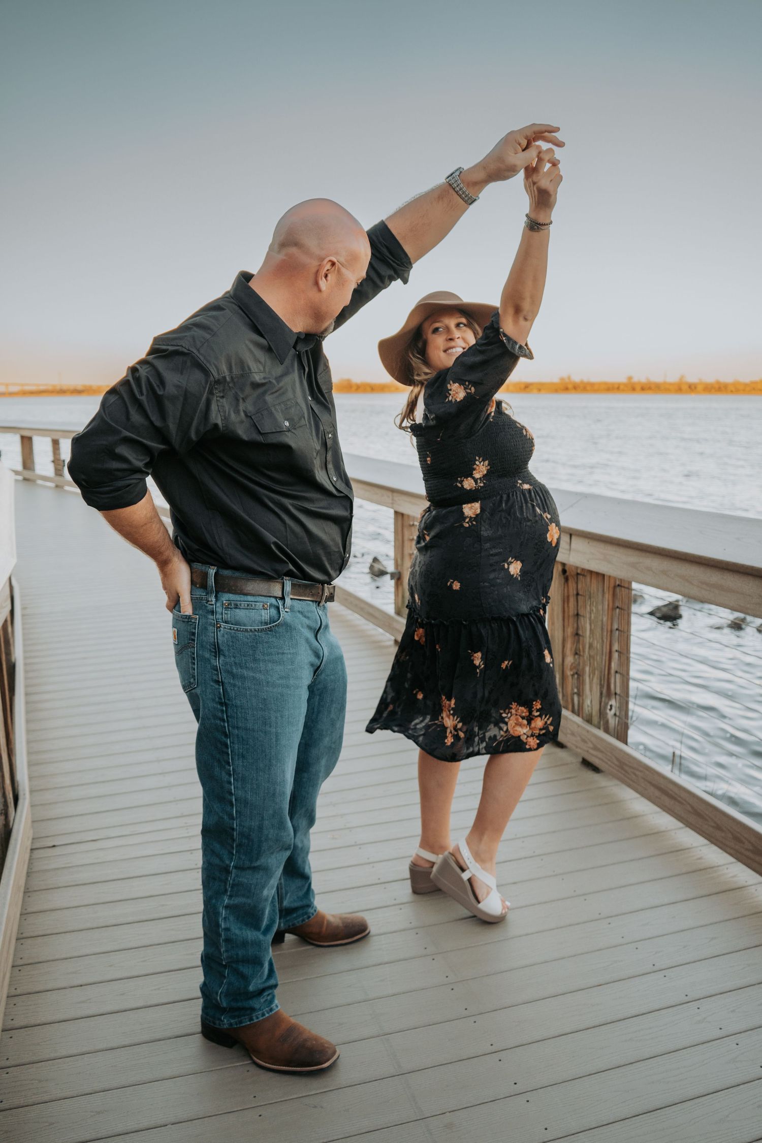 A couple dancing together on a waterfront deck at sunset.