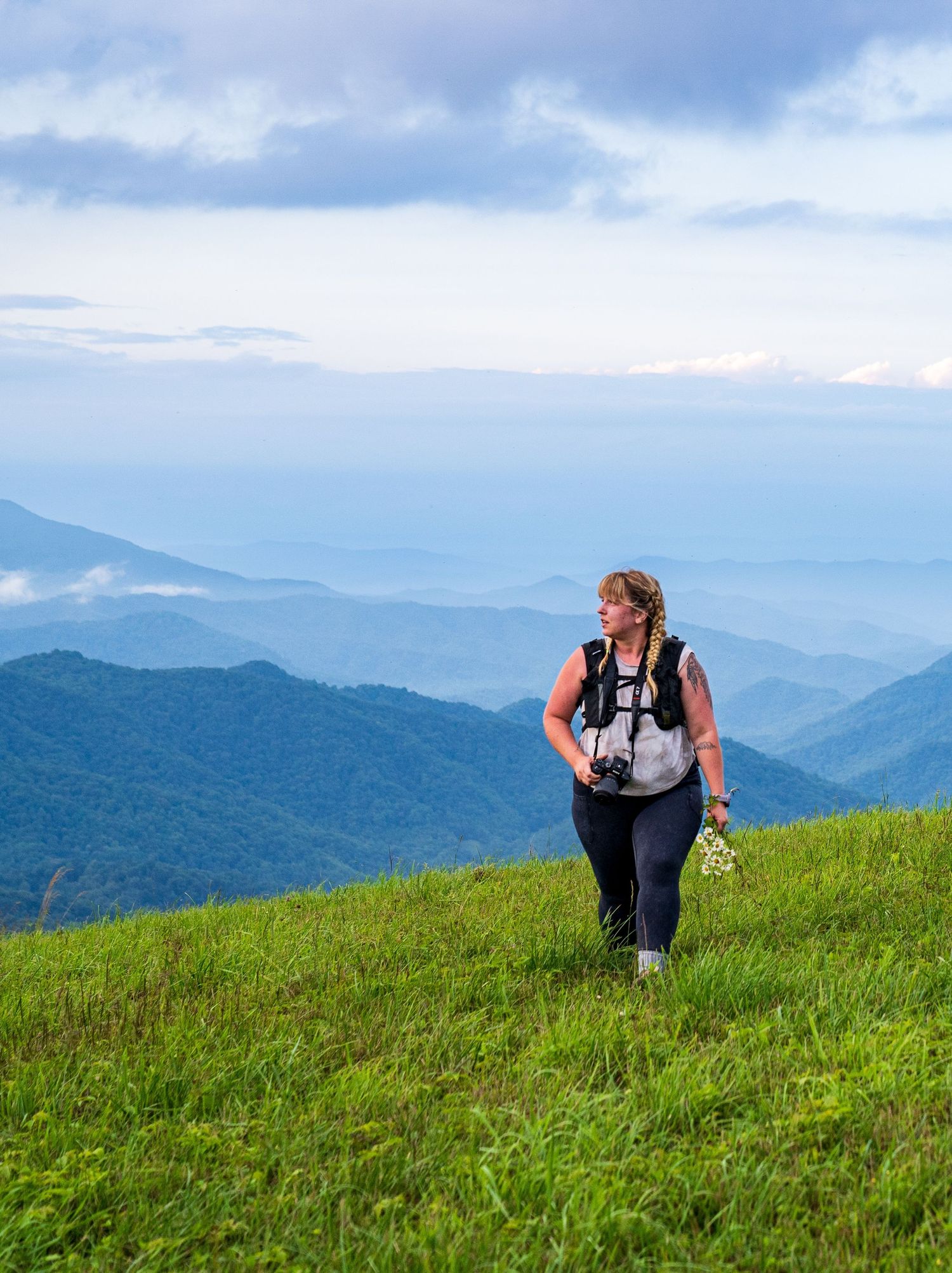 A hiker walks along a grassy mountain ridge with misty blue mountains in the distance.