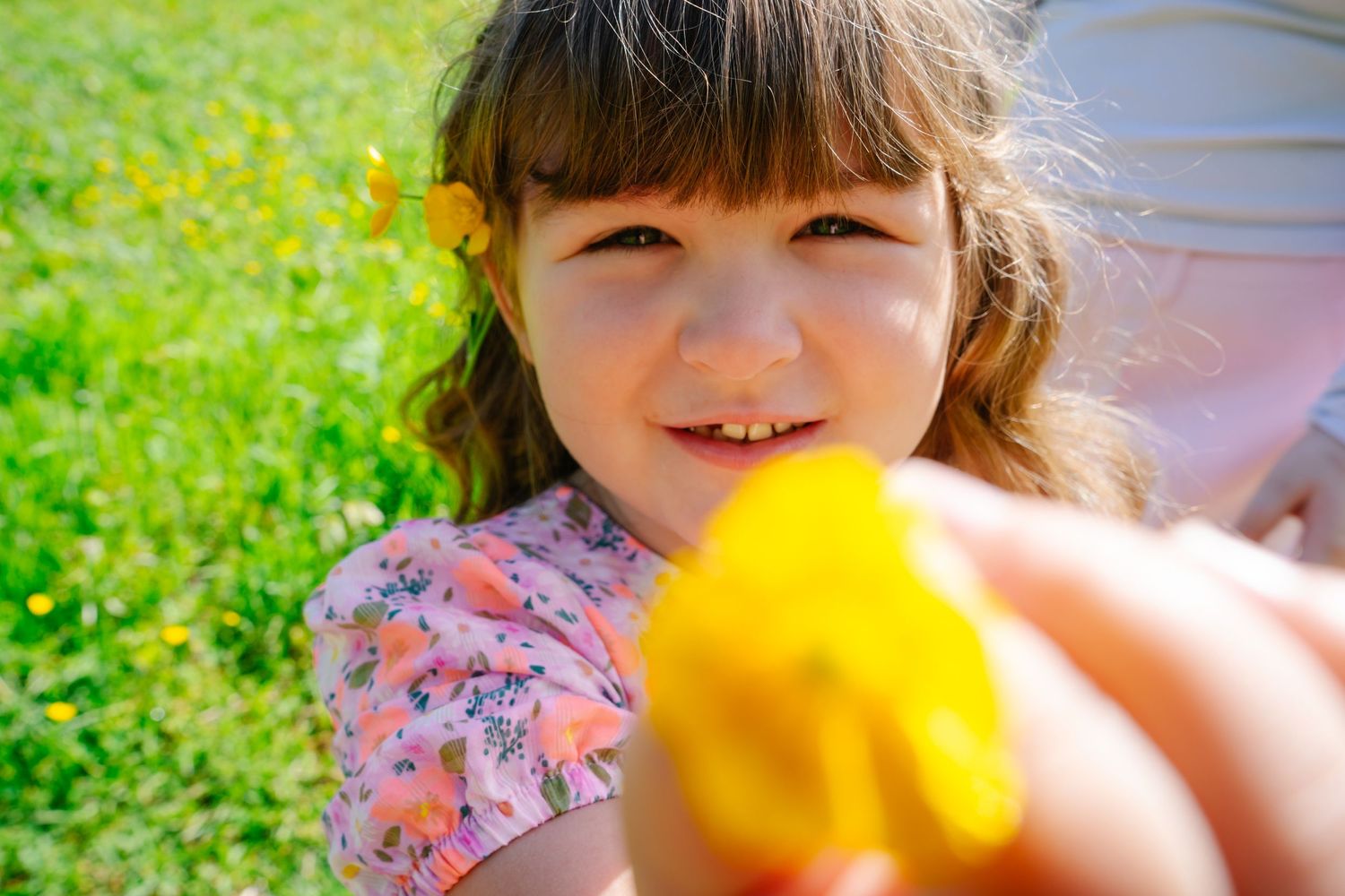 Close up of child with bangs smiling at yellow object in sunlit outdoor setting.