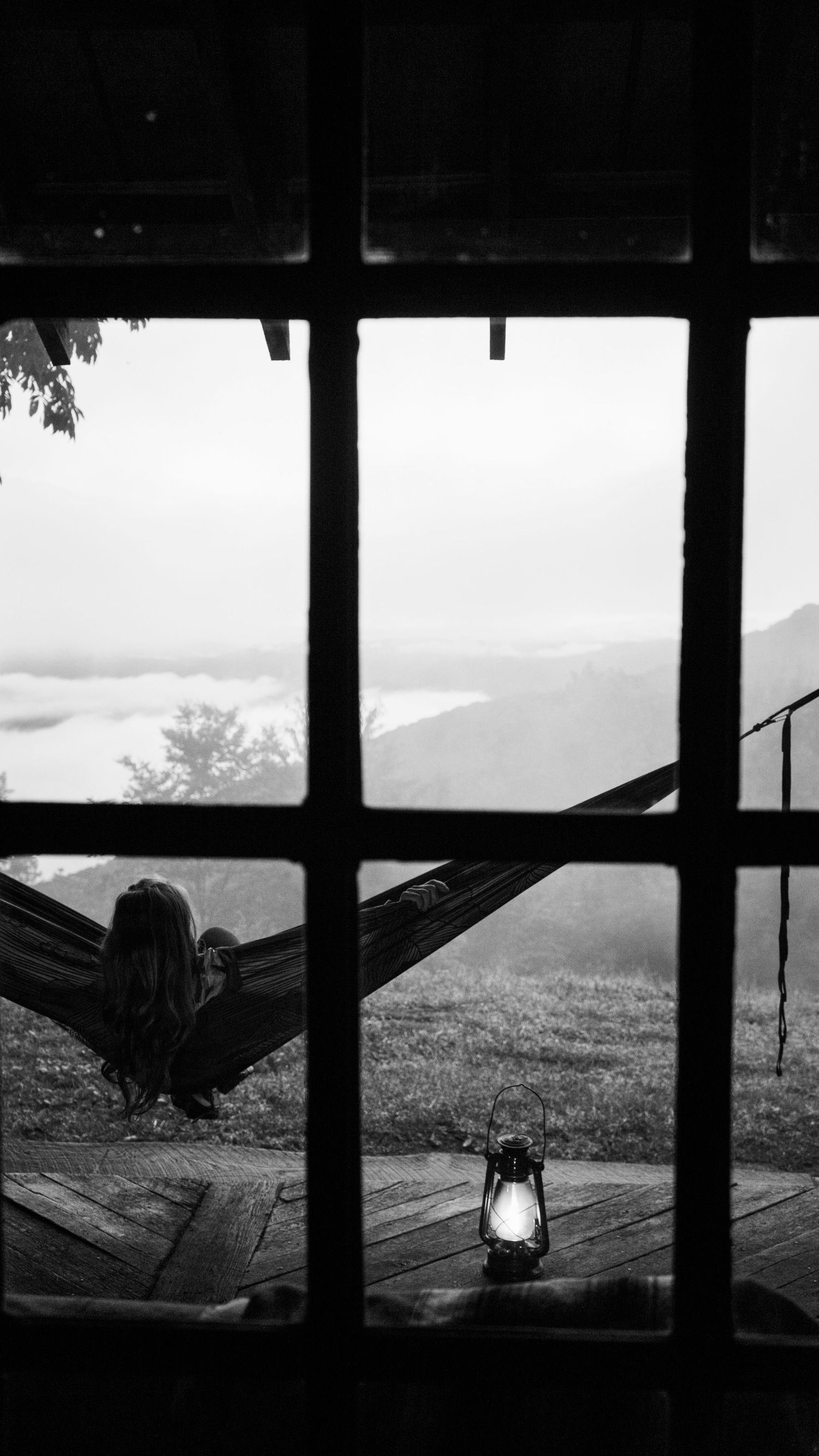 A silhouetted view through a window shows hammocks hanging in a rustic cabin with mountains visible in the background.