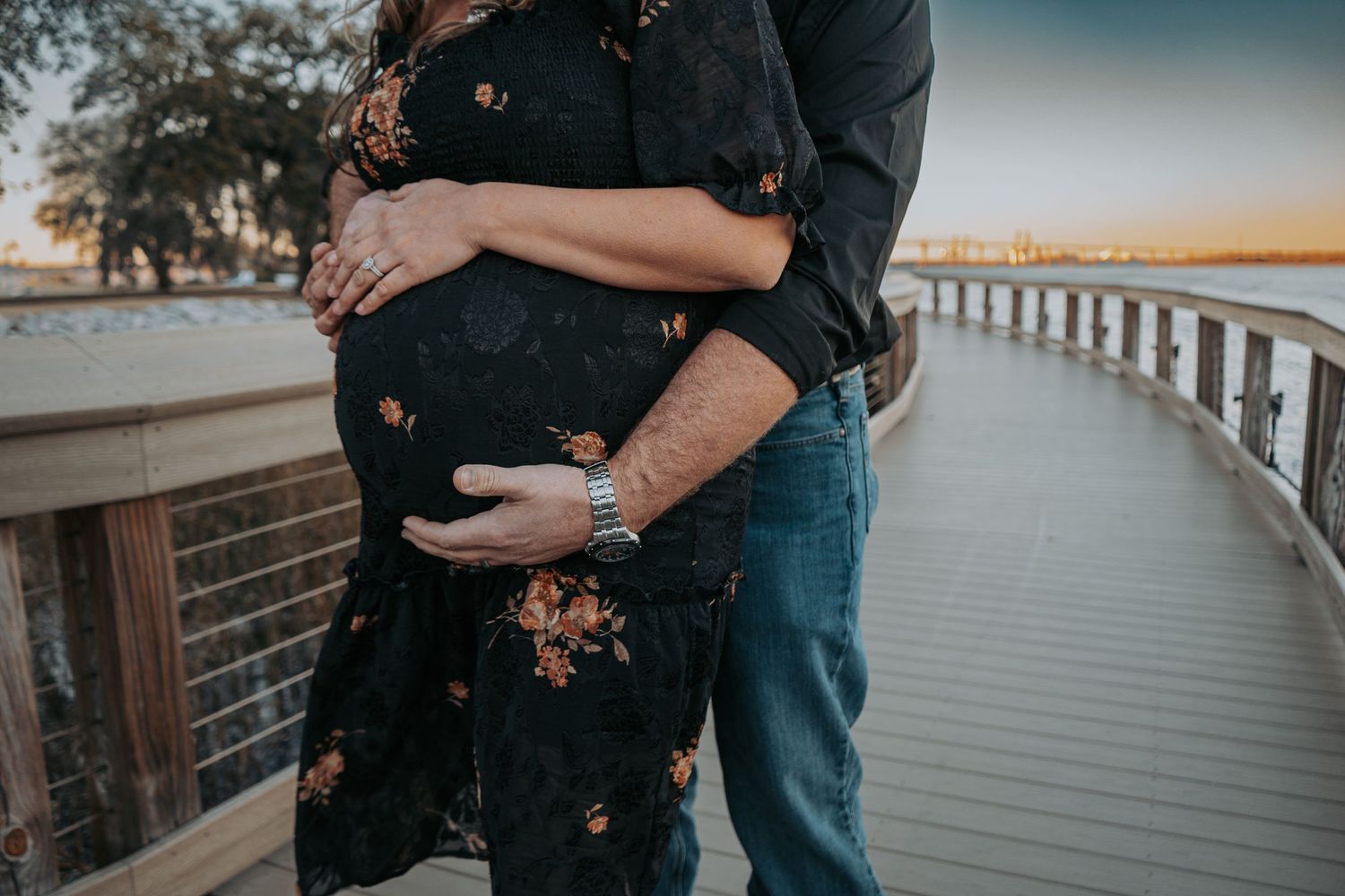 A tender embrace captured on a curved wooden boardwalk near the water.