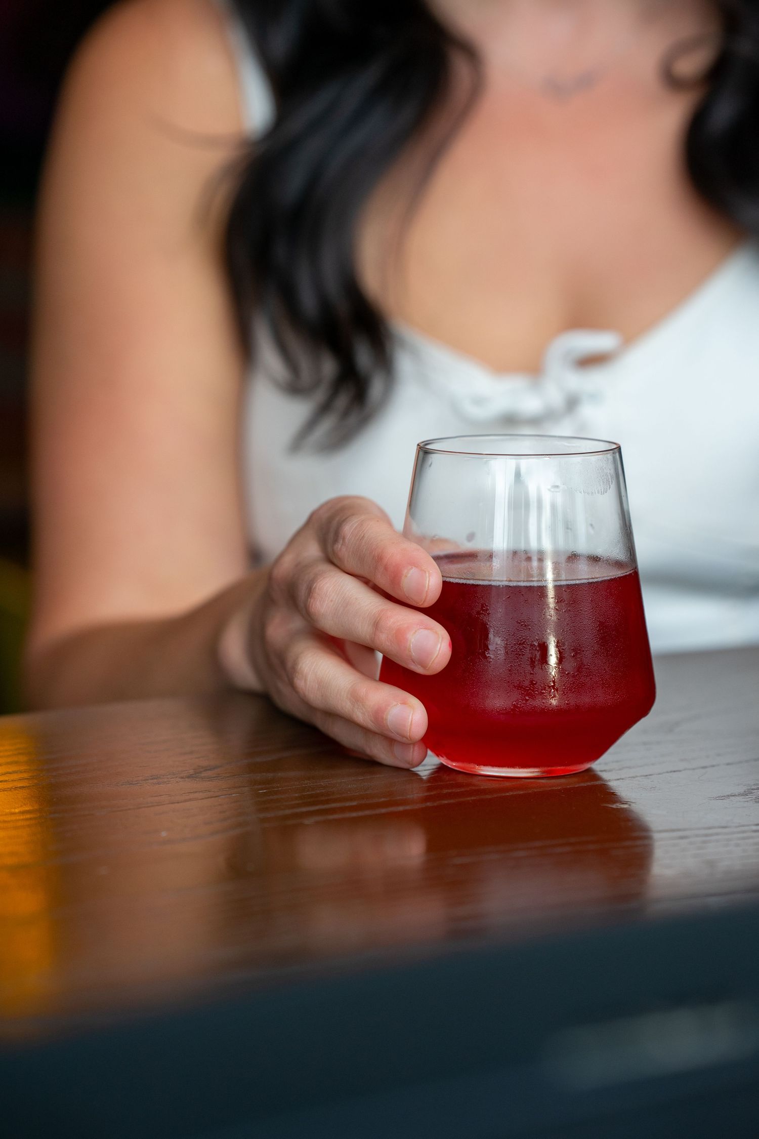 A sequence of shots showing a glass of red cocktail being slid across a dark wooden table.