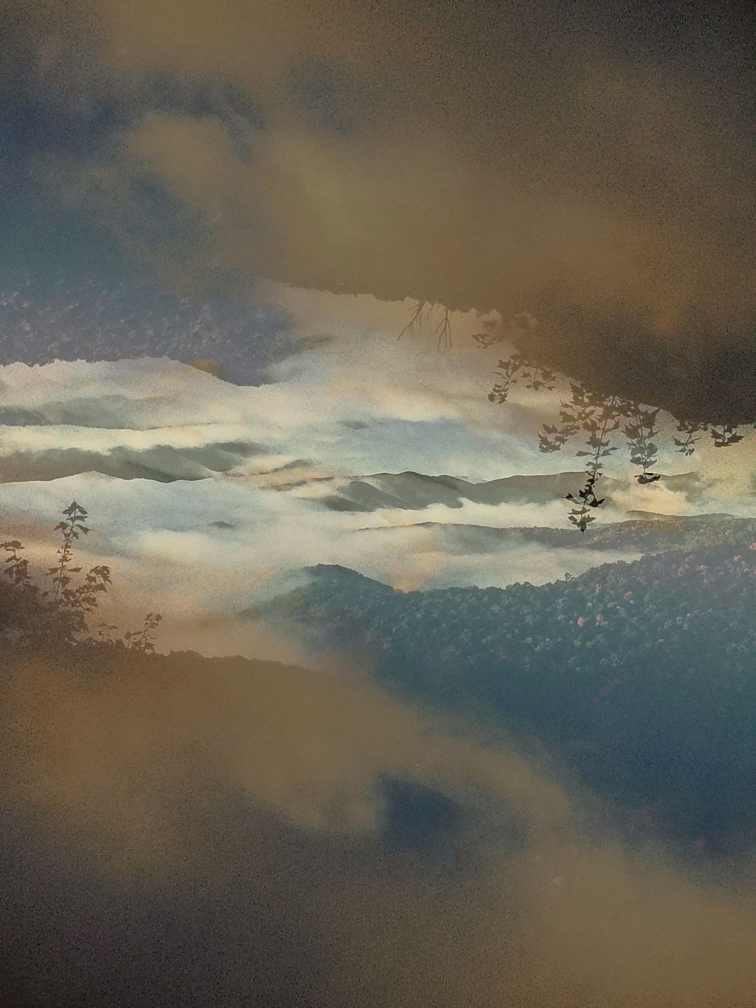 Dramatic mountain landscape with misty clouds and silhouetted trees against a moody sky at sunset.