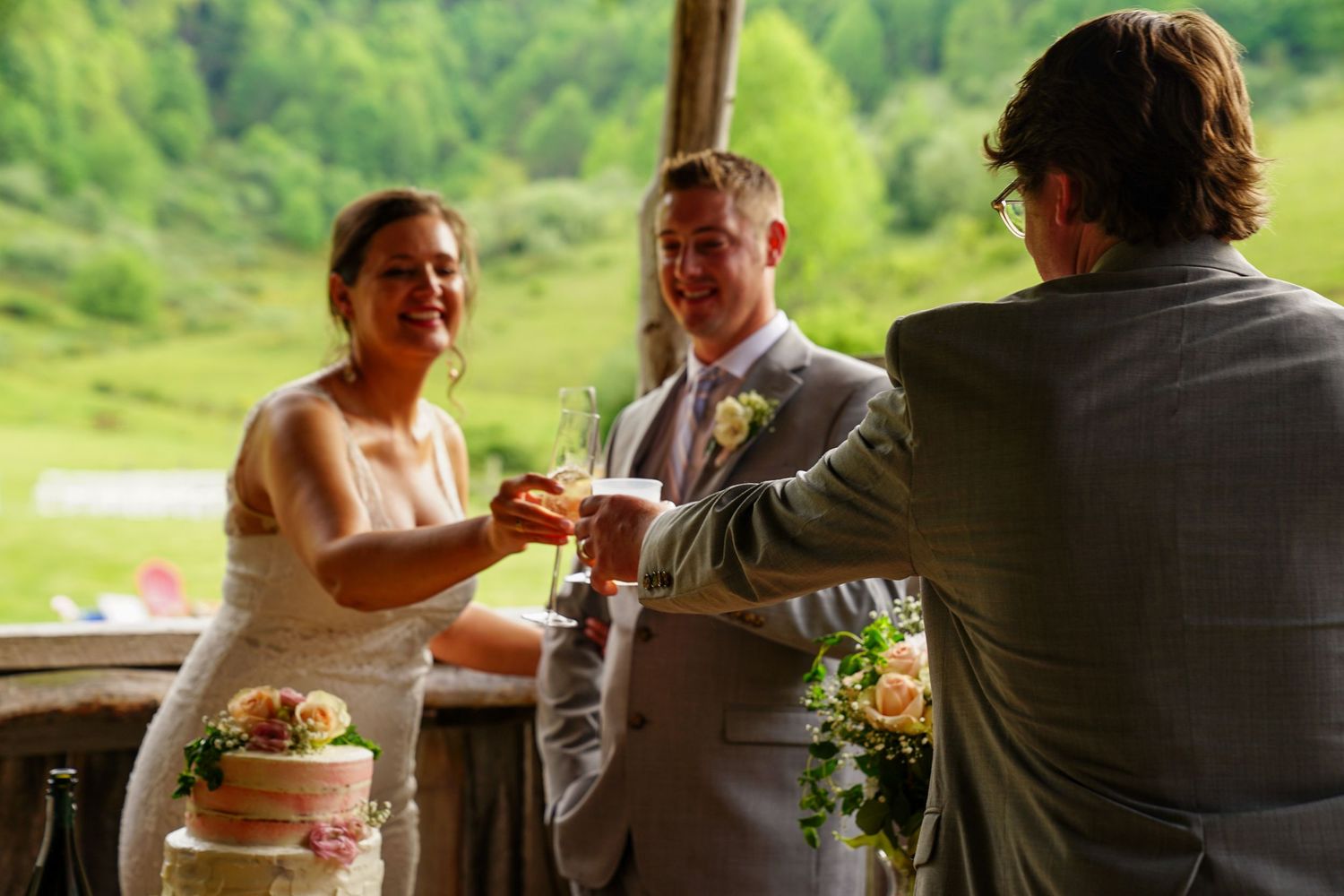 A newlywed couple cuts into their white wedding cake together at an outdoor reception venue.