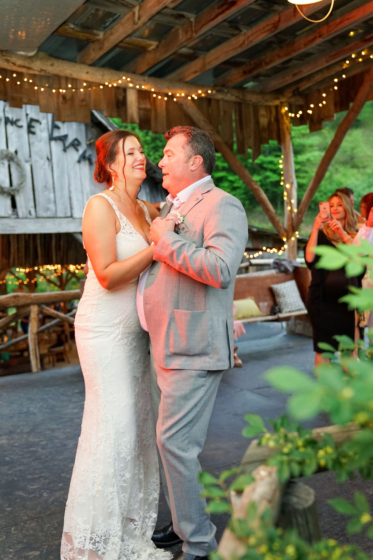 A couple shares their first dance together at a rustic barn wedding reception decorated with twinkling lights.