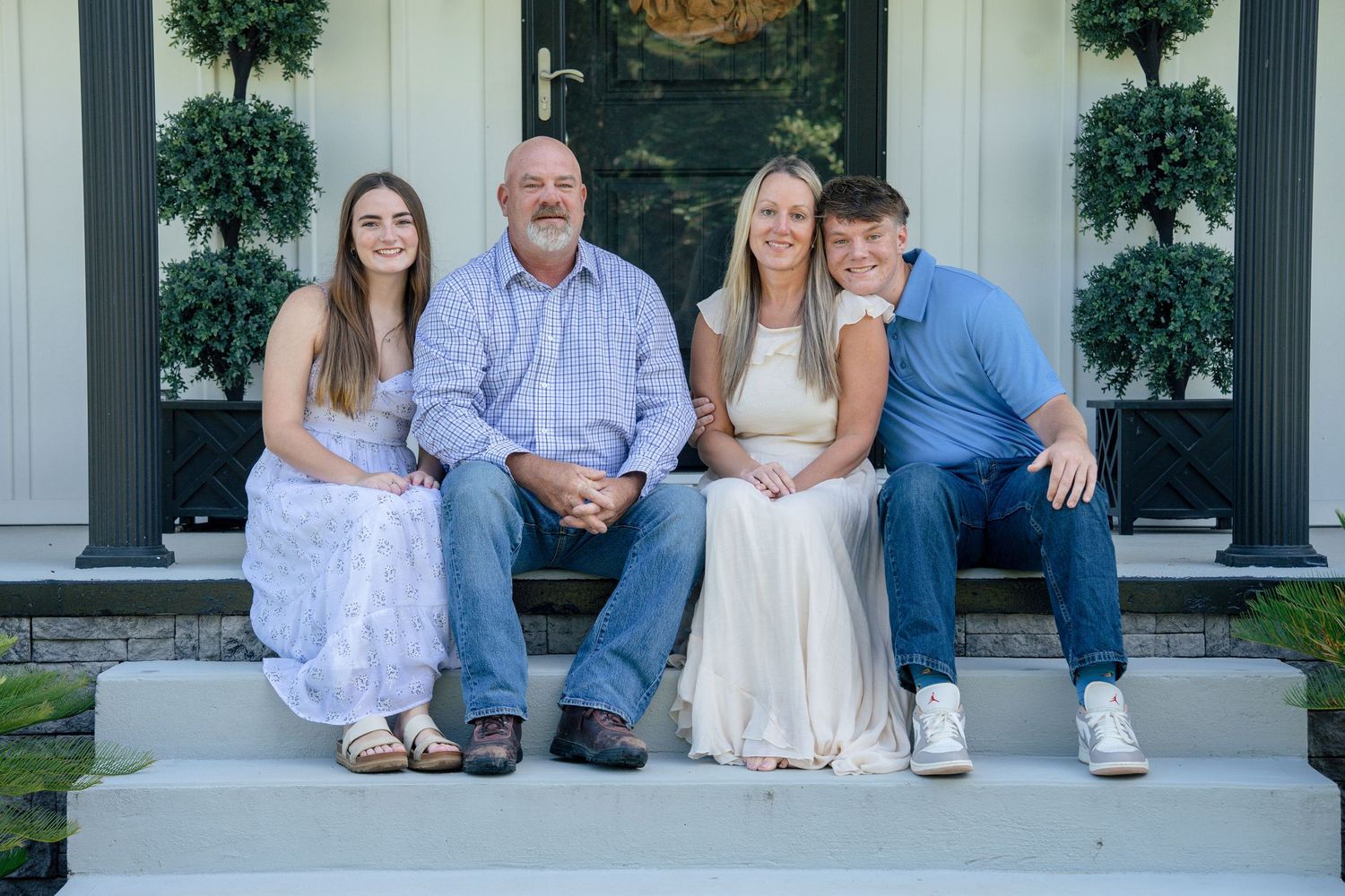 A family wearing coordinated blue and white outfits sits together on outdoor porch steps for a portrait.