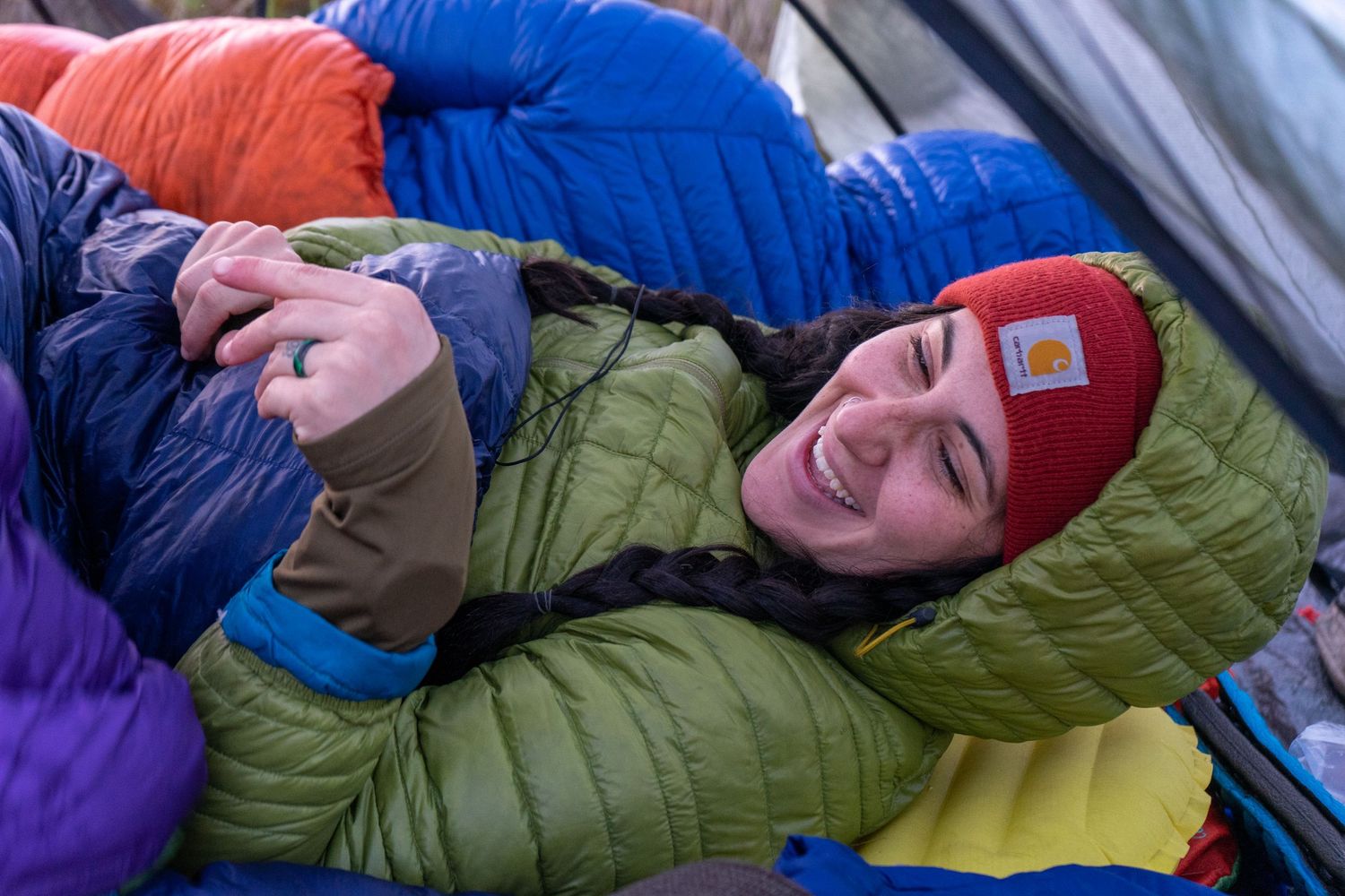 Camper resting in colorful sleeping bags inside tent during winter expedition.